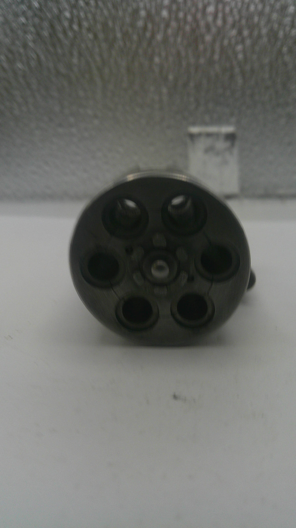 Black cylindrical object with multiple holes on a textured surface