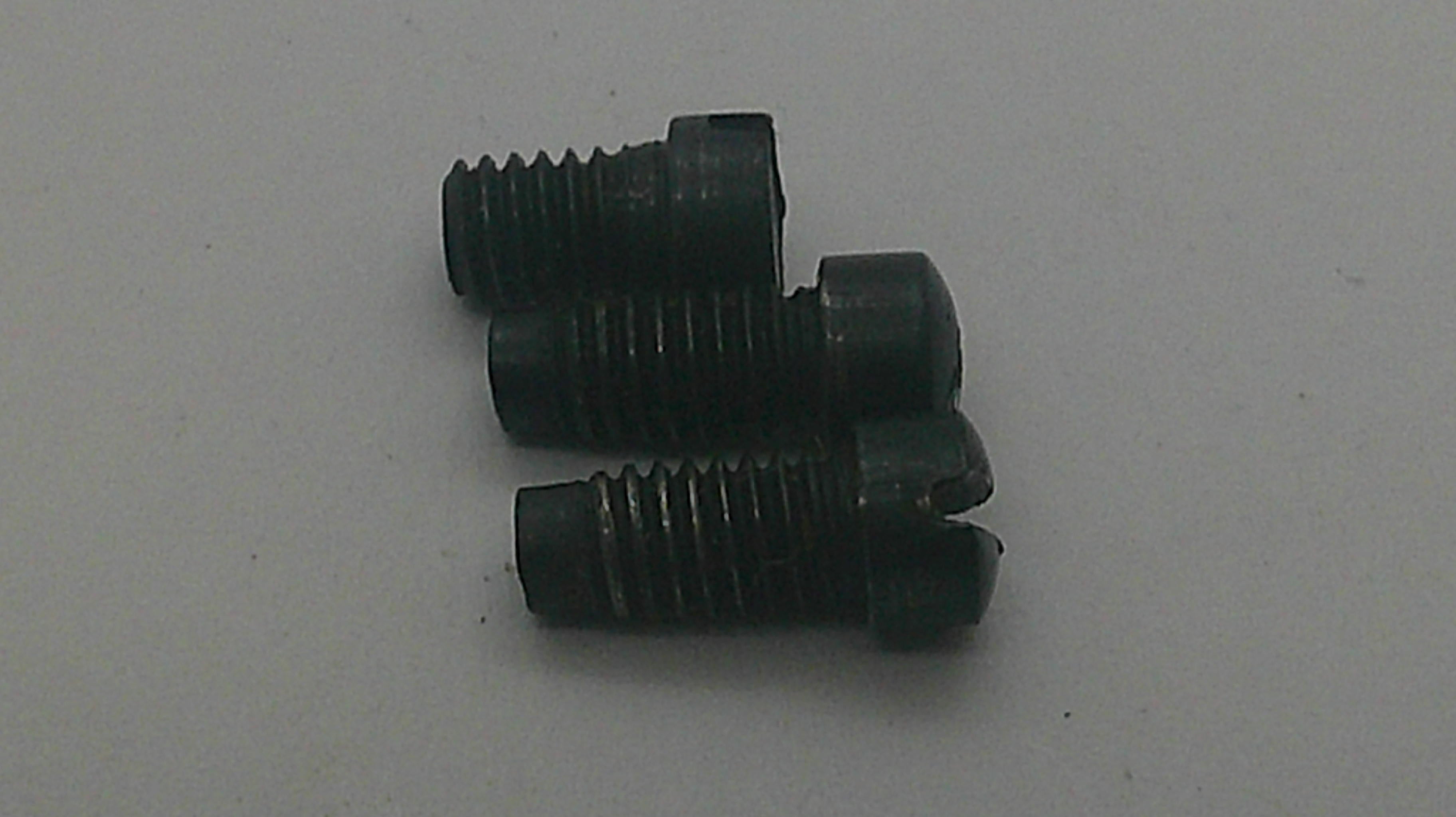 Three small black threaded screws with slotted countersunk heads, arranged vertically on a plain light gray surface.