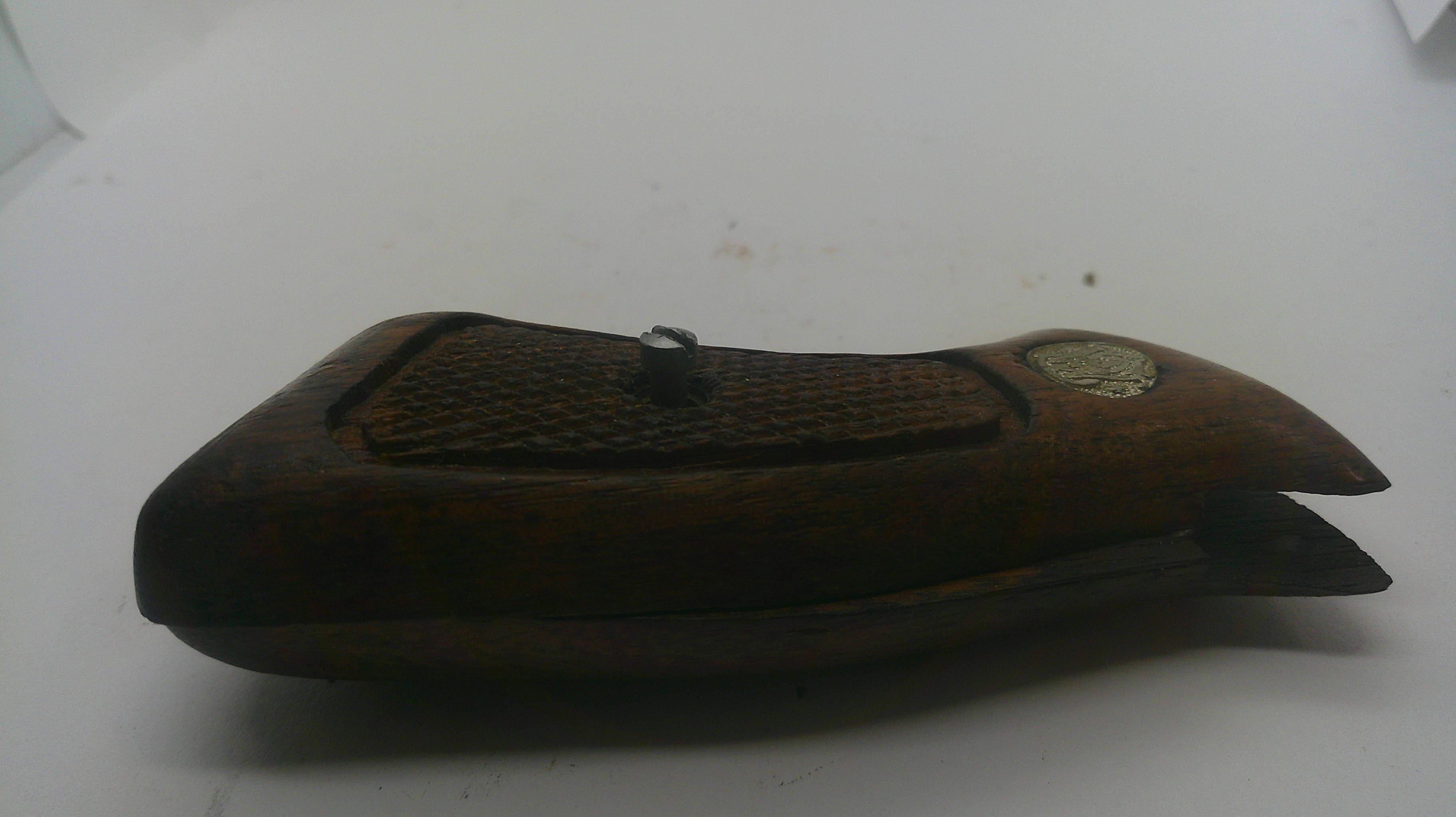 A dark brown wooden case with a textured grip pattern and a small round metallic emblem, photographed on a plain white surface.