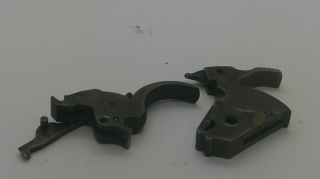 Two dark metal firearm trigger components photographed on a plain light background.