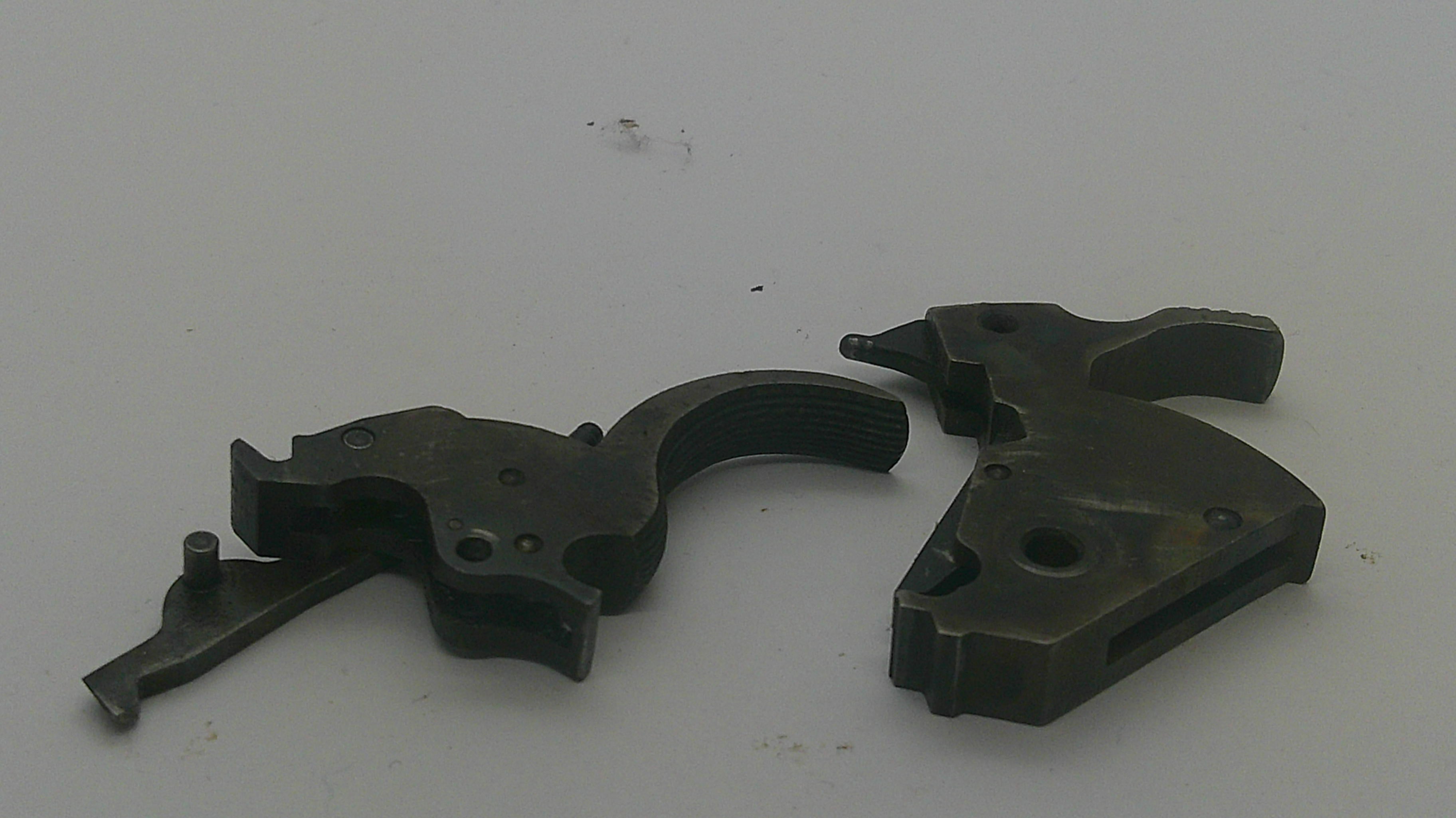 Two dark metal firearm trigger components photographed on a plain light background.