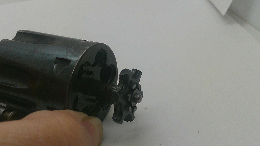 A close-up of a black metal revolver cylinder with the hammer removed, held by a person's fingers against a plain white background.
