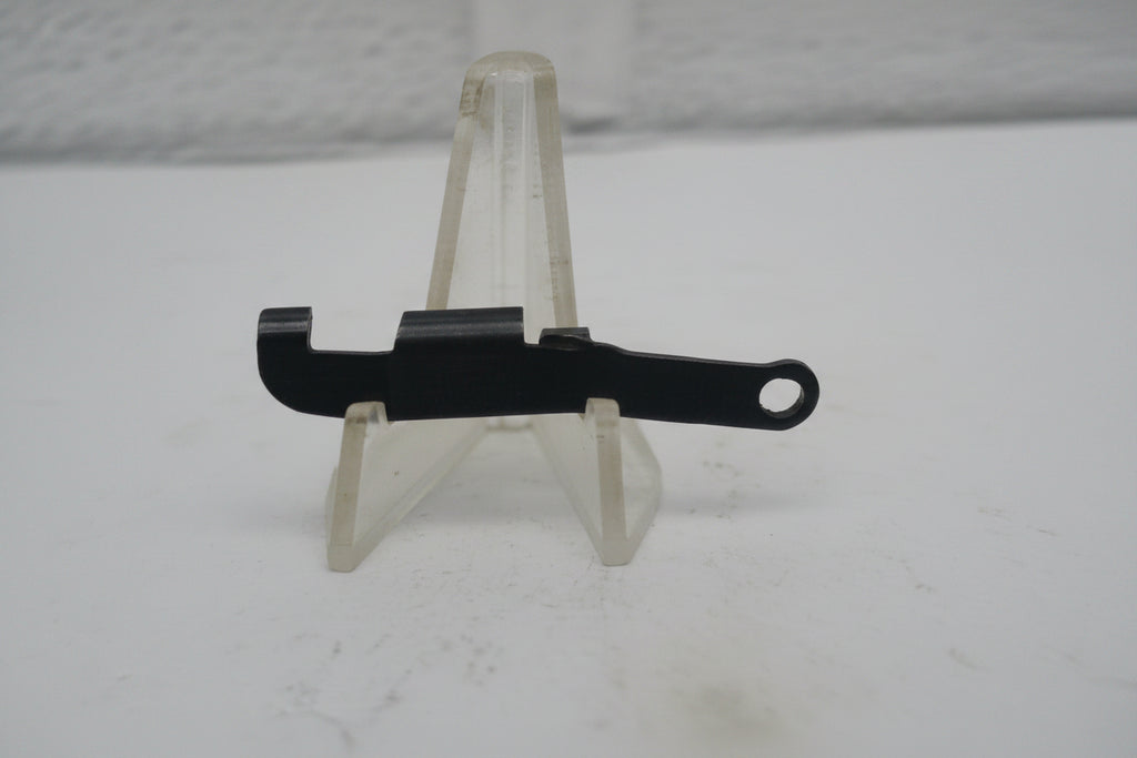A small black plastic mechanical part or clip displayed on a clear plastic stand against a plain light background.