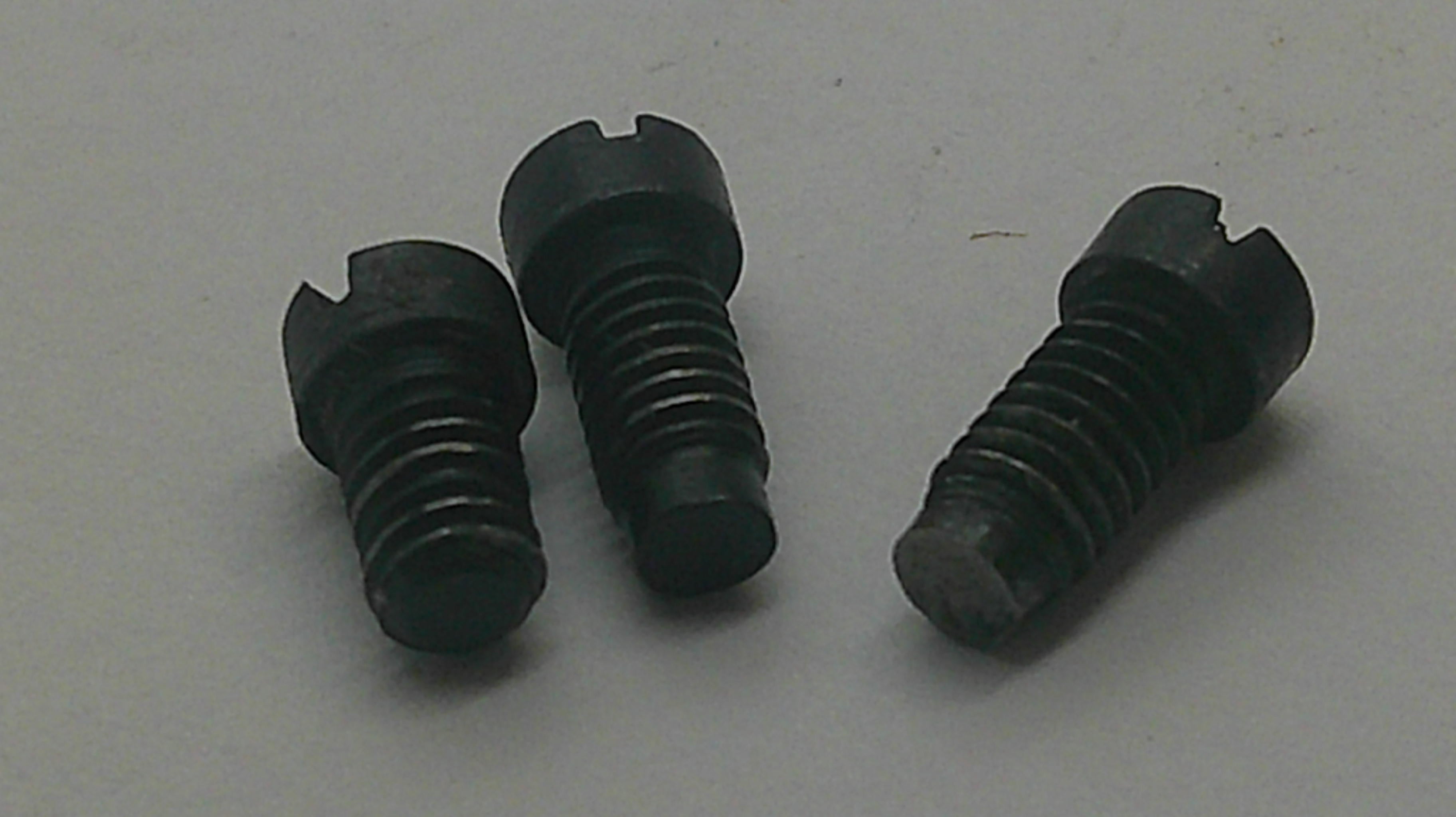 Three small black threaded metal screws or bolts with slotted heads, arranged on a plain light gray surface.