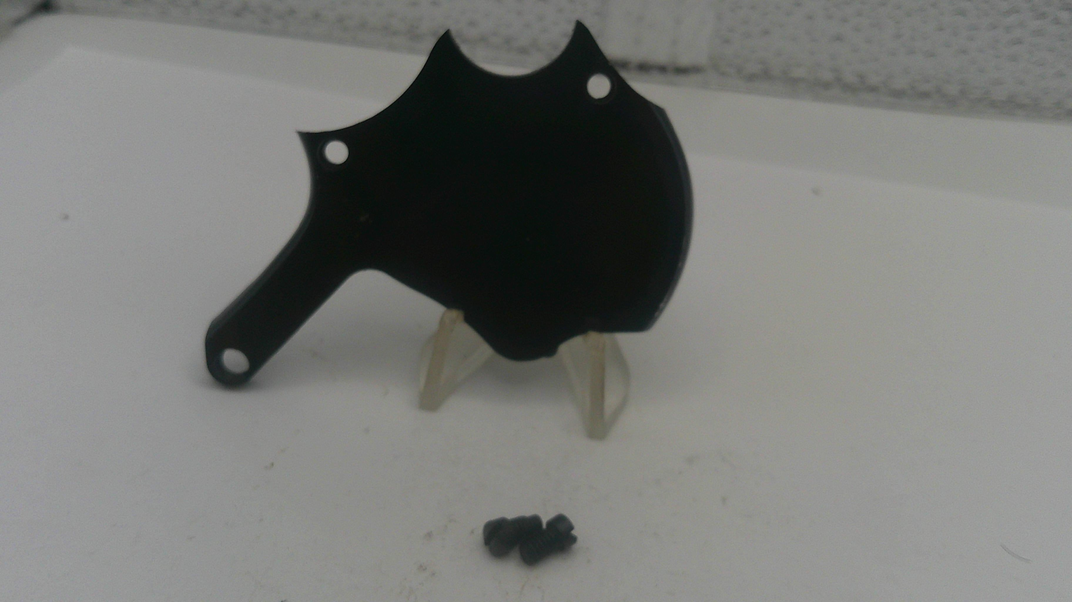 Black metal object on a stand with small black components on a white surface