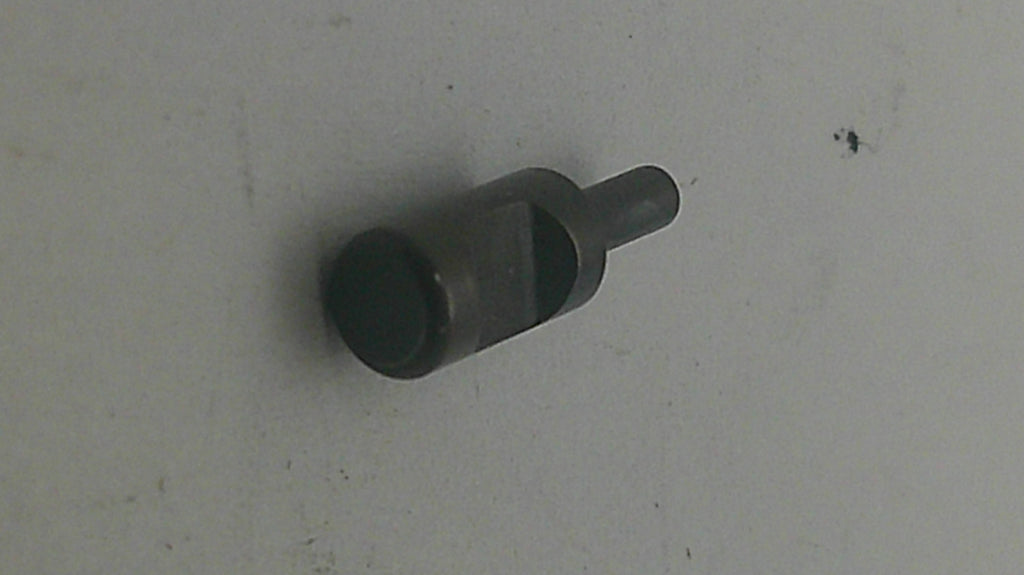 A small dark metal cylindrical tool or hardware piece with a flat circular end and a short protruding shaft, photographed on a plain light surface.