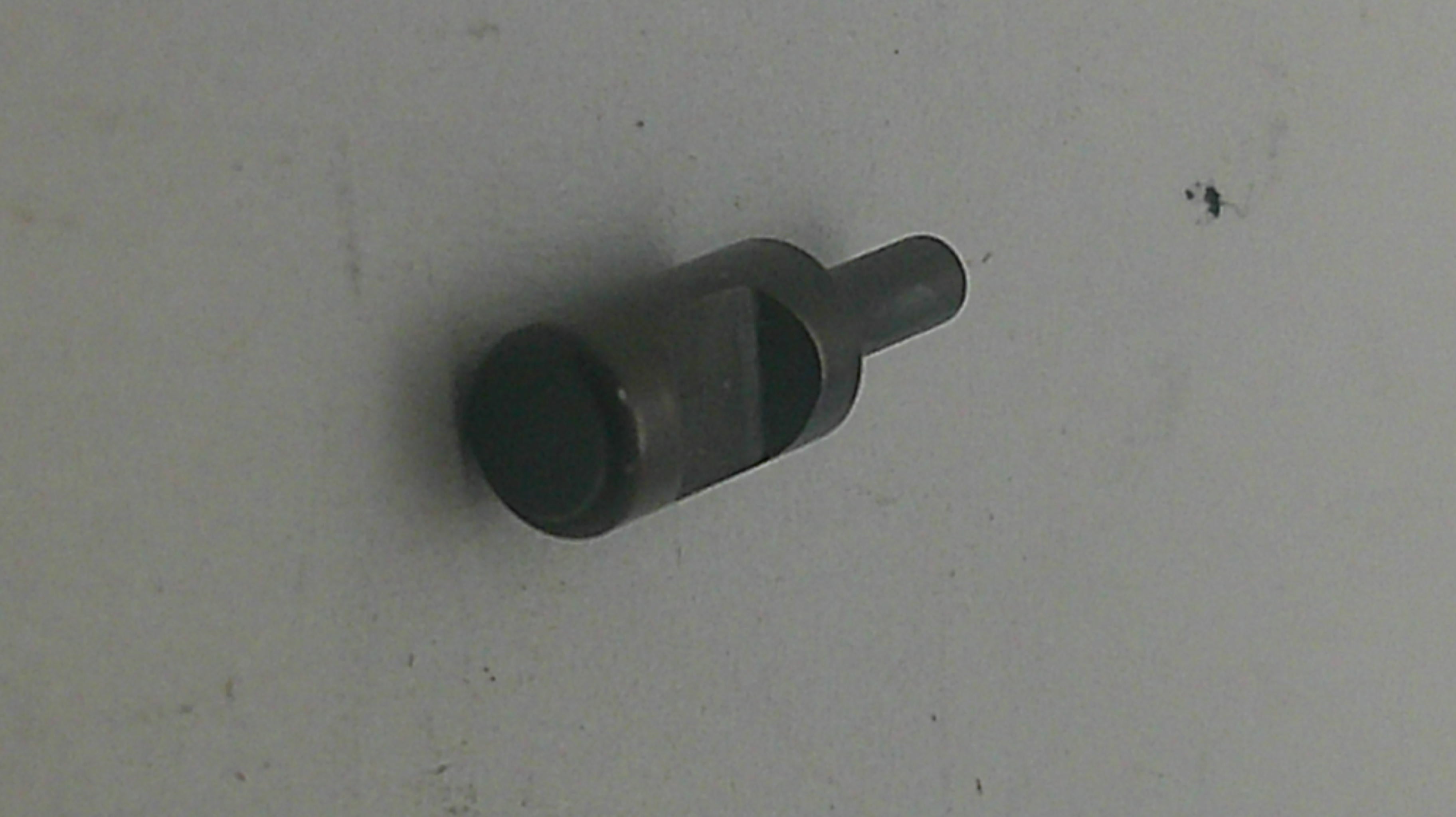 A small dark metal cylindrical tool or hardware piece with a flat circular end and a short protruding shaft, photographed on a plain light surface.