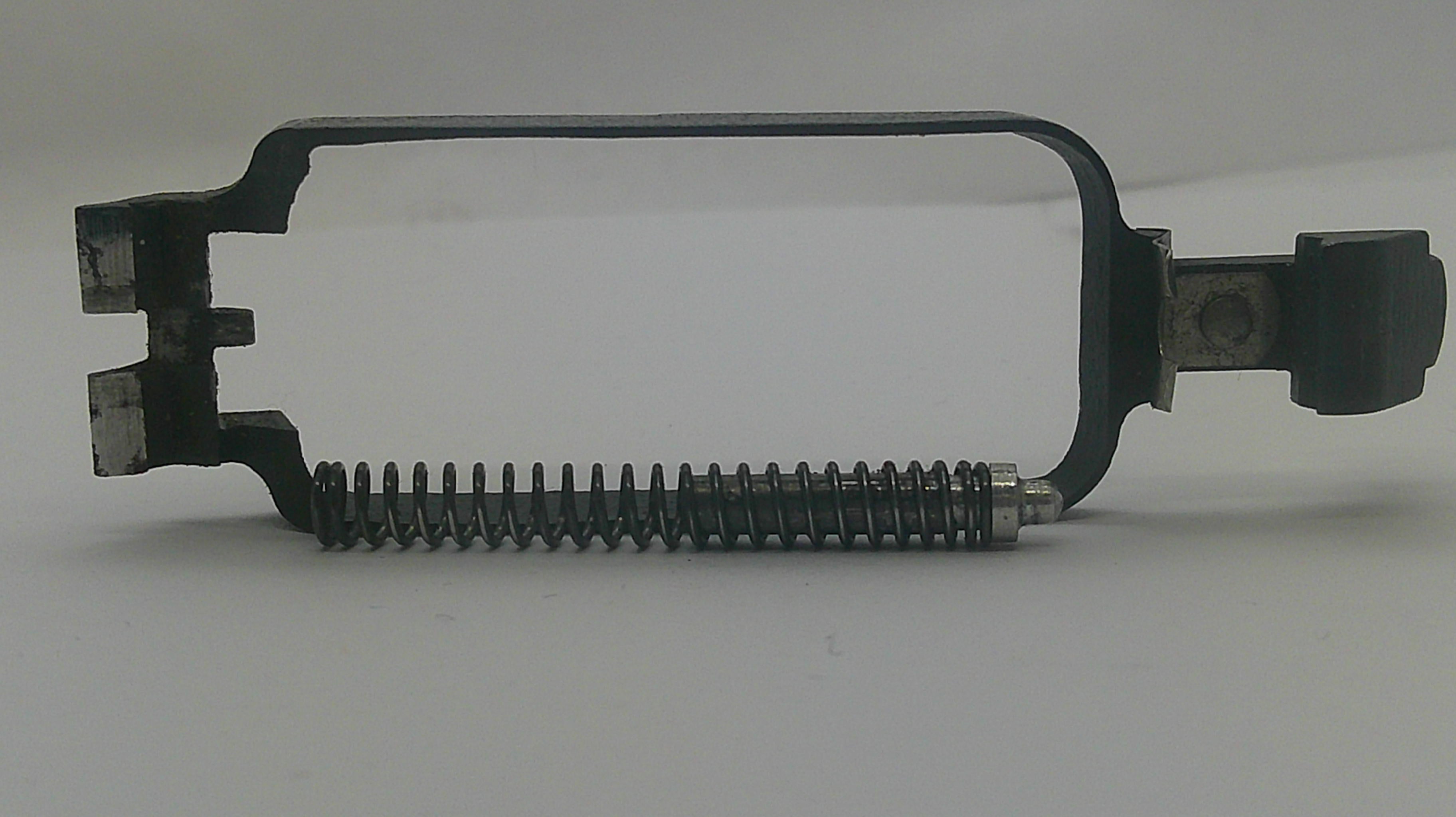 A black metal mechanical component with a coiled spring and a small black knob, photographed on a plain light background.