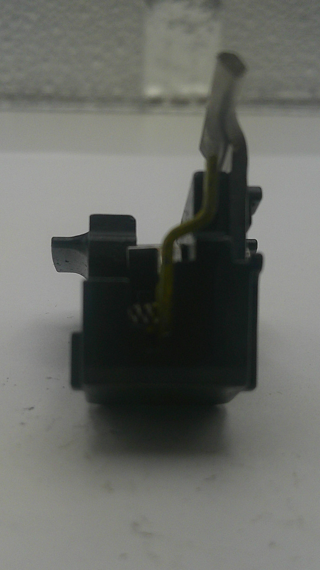 A close-up of a black plastic electronic switch component with a yellow wire attached, photographed against a white surface.
