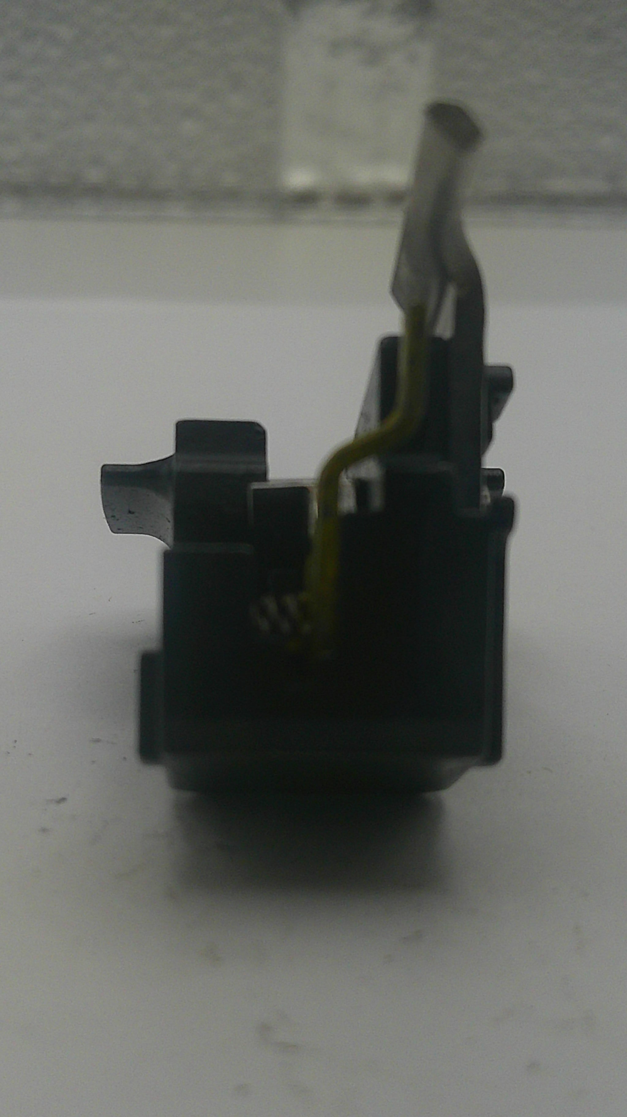 A close-up of a black plastic electronic switch component with a yellow wire attached, photographed against a white surface.