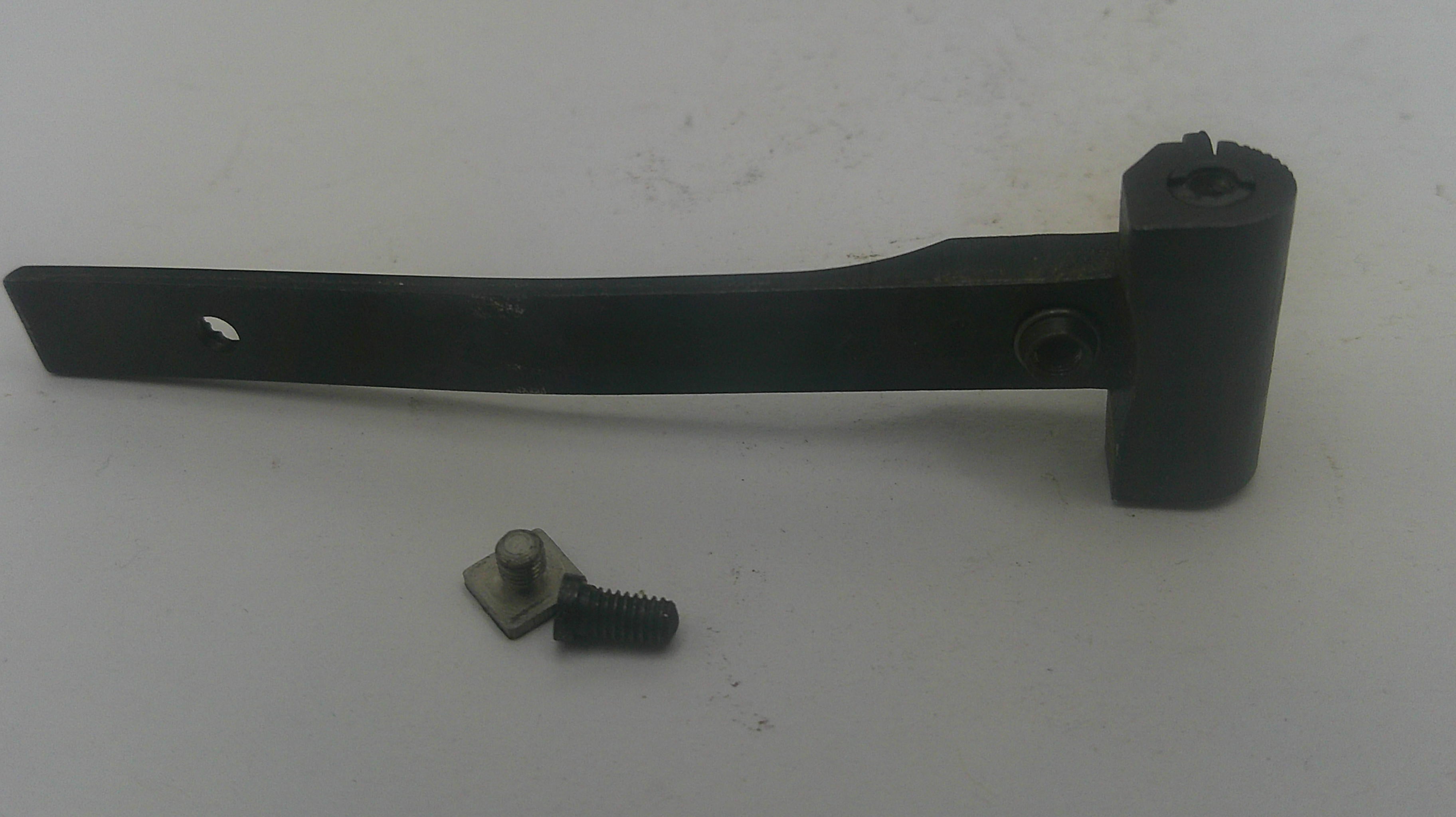 A black metal hinge or bracket with a cylindrical mounting piece and a small loose screw and bolt placed below it, photographed on a plain off-white surface.