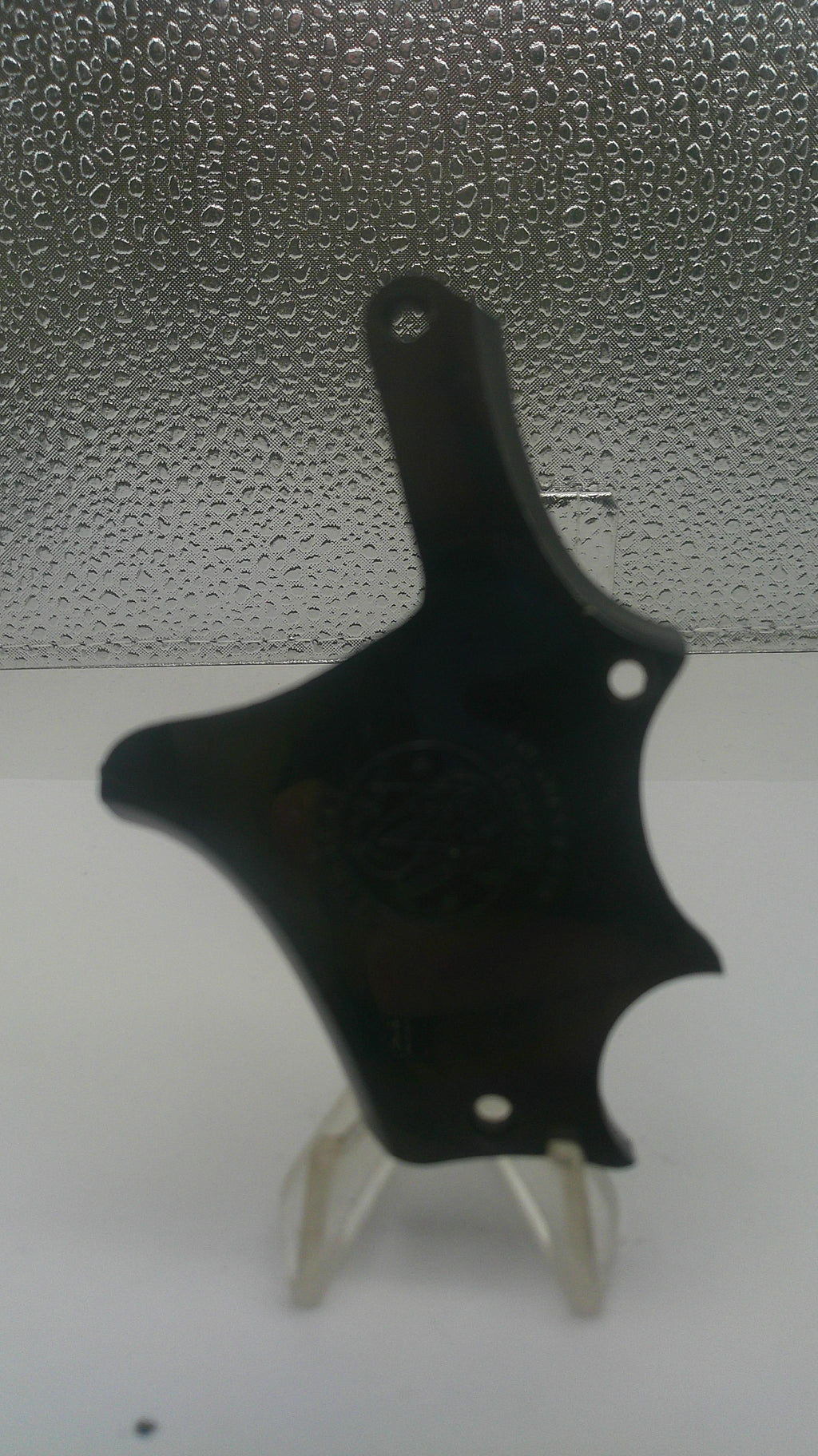 A black plastic multi-tool with a star-shaped head and a small white plastic lever, shown against a split white and textured gray background.