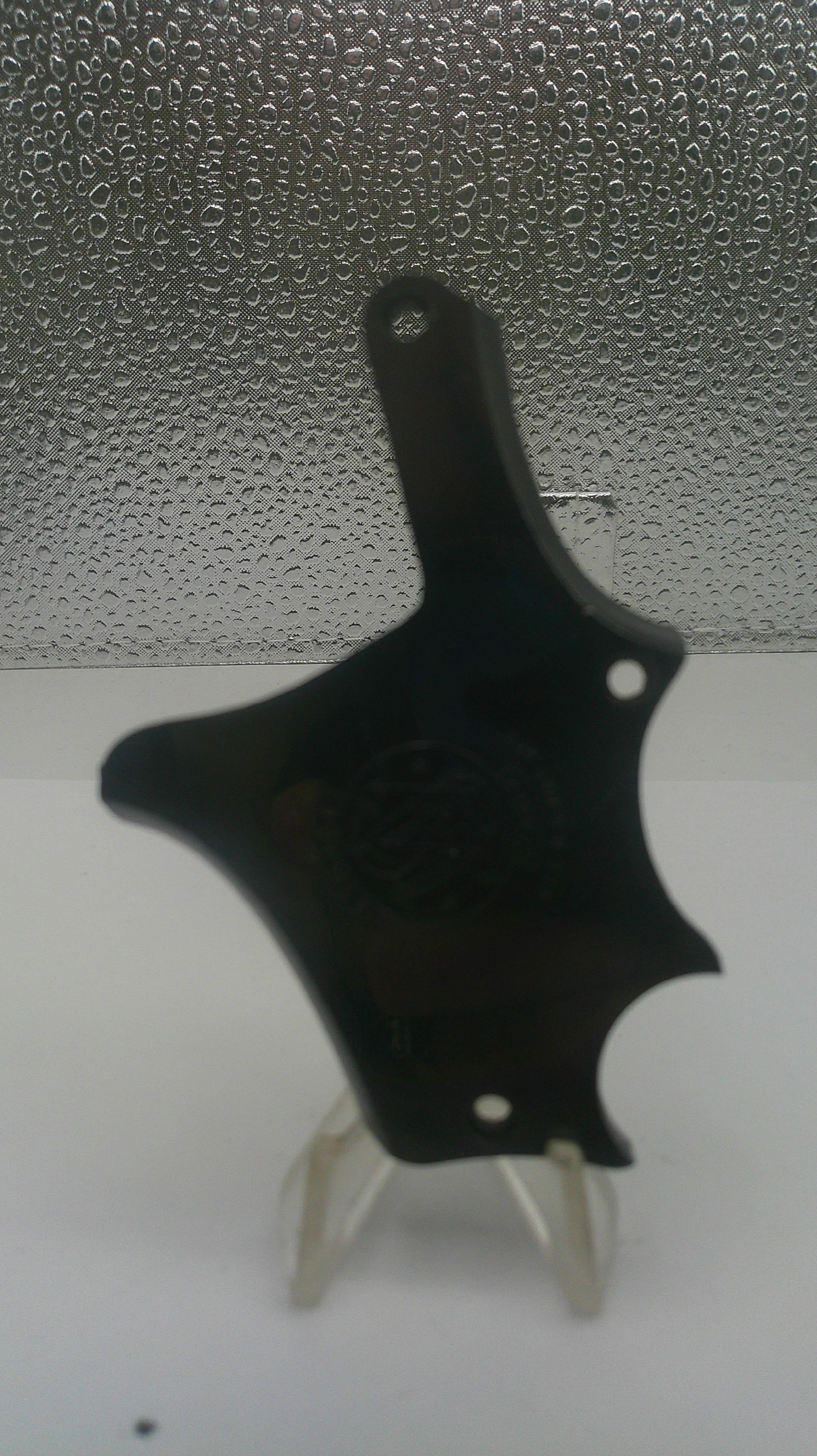 A black plastic multi-tool with a star-shaped head and a small white plastic lever, shown against a split white and textured gray background.