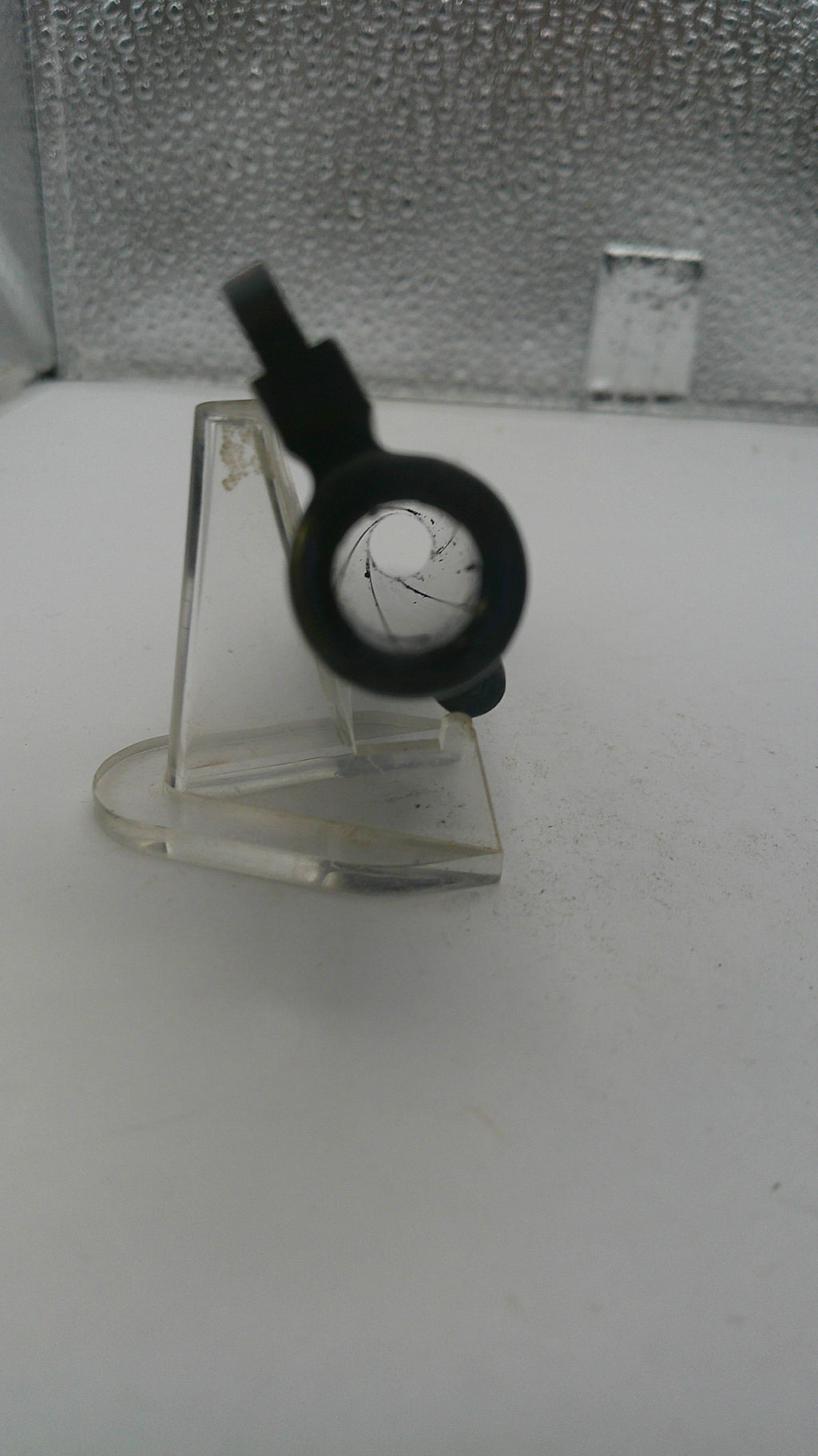 Clear plastic stand with a black object on a textured surface