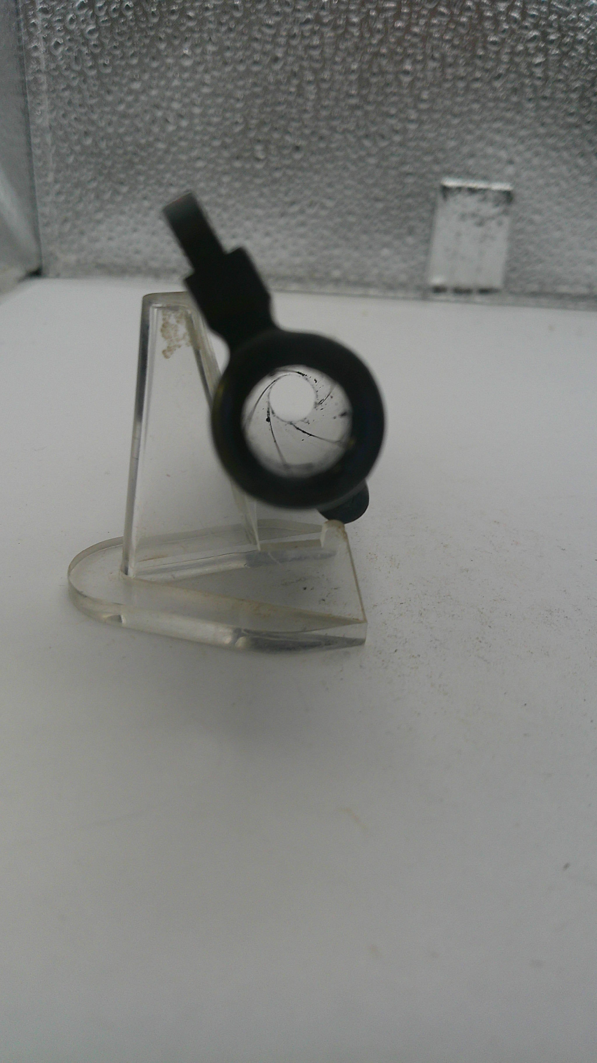 Clear plastic stand with a black object on a textured surface