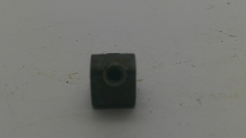 A small dark metal cylindrical component with a threaded hole, placed on a light gray surface.