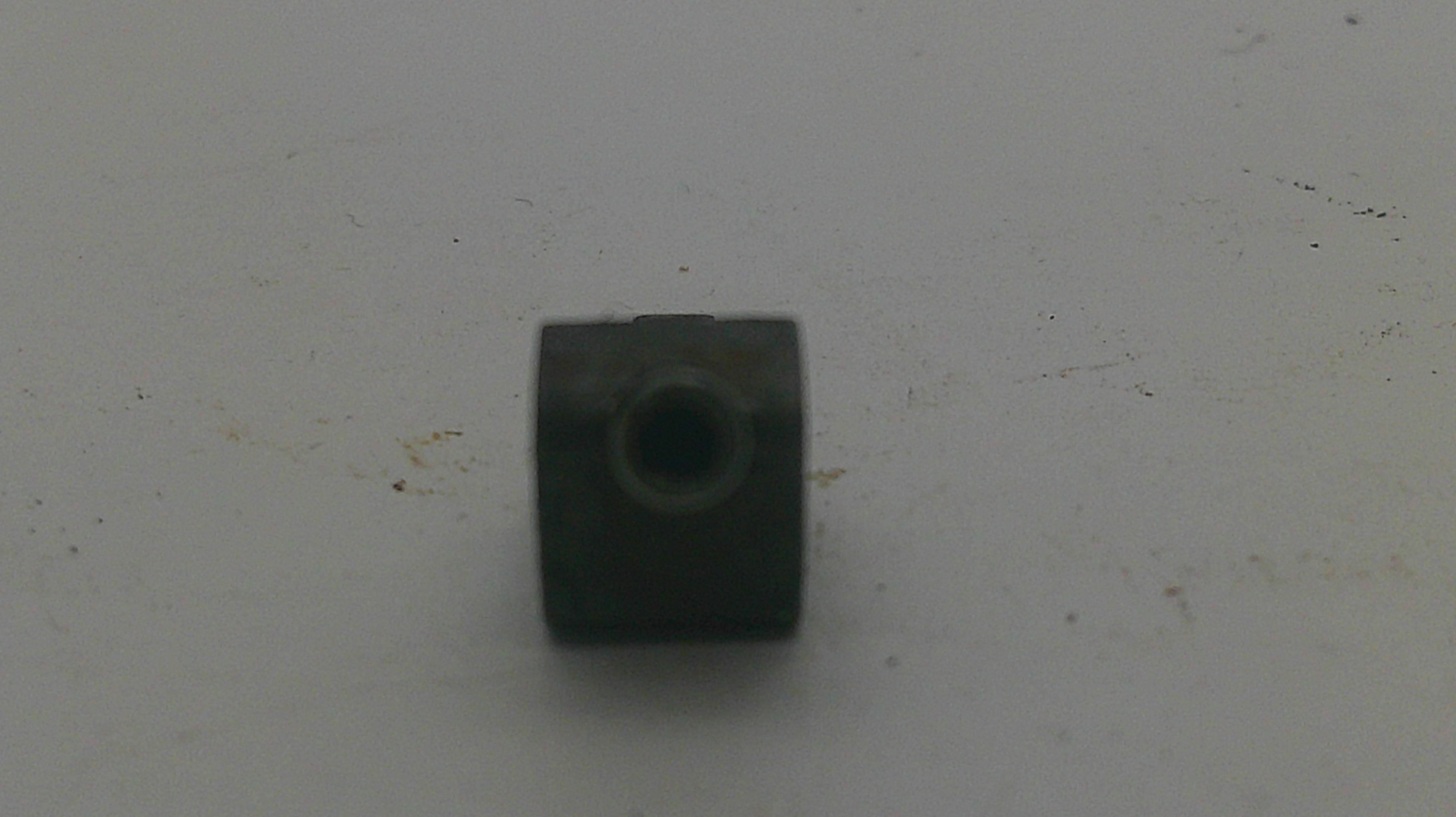 A small dark metal cylindrical component with a threaded hole, placed on a light gray surface.