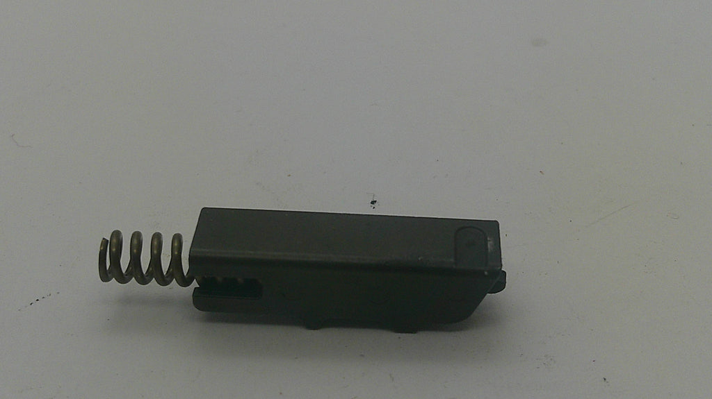 A small black plastic component with a metal coil spring attached to one end, photographed on a plain light background.