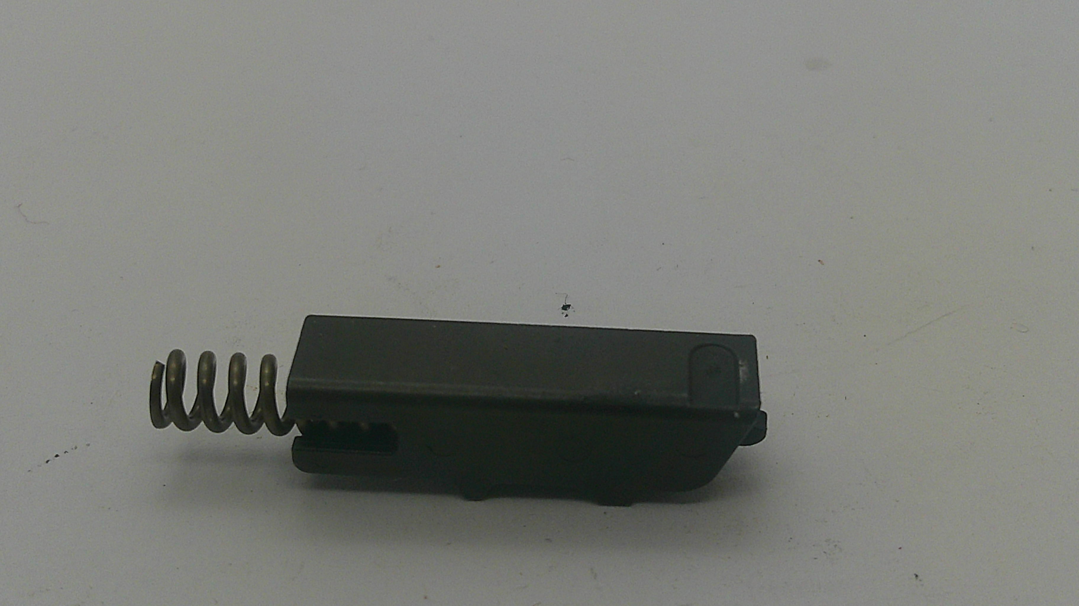 A small black plastic component with a metal coil spring attached to one end, photographed on a plain light background.