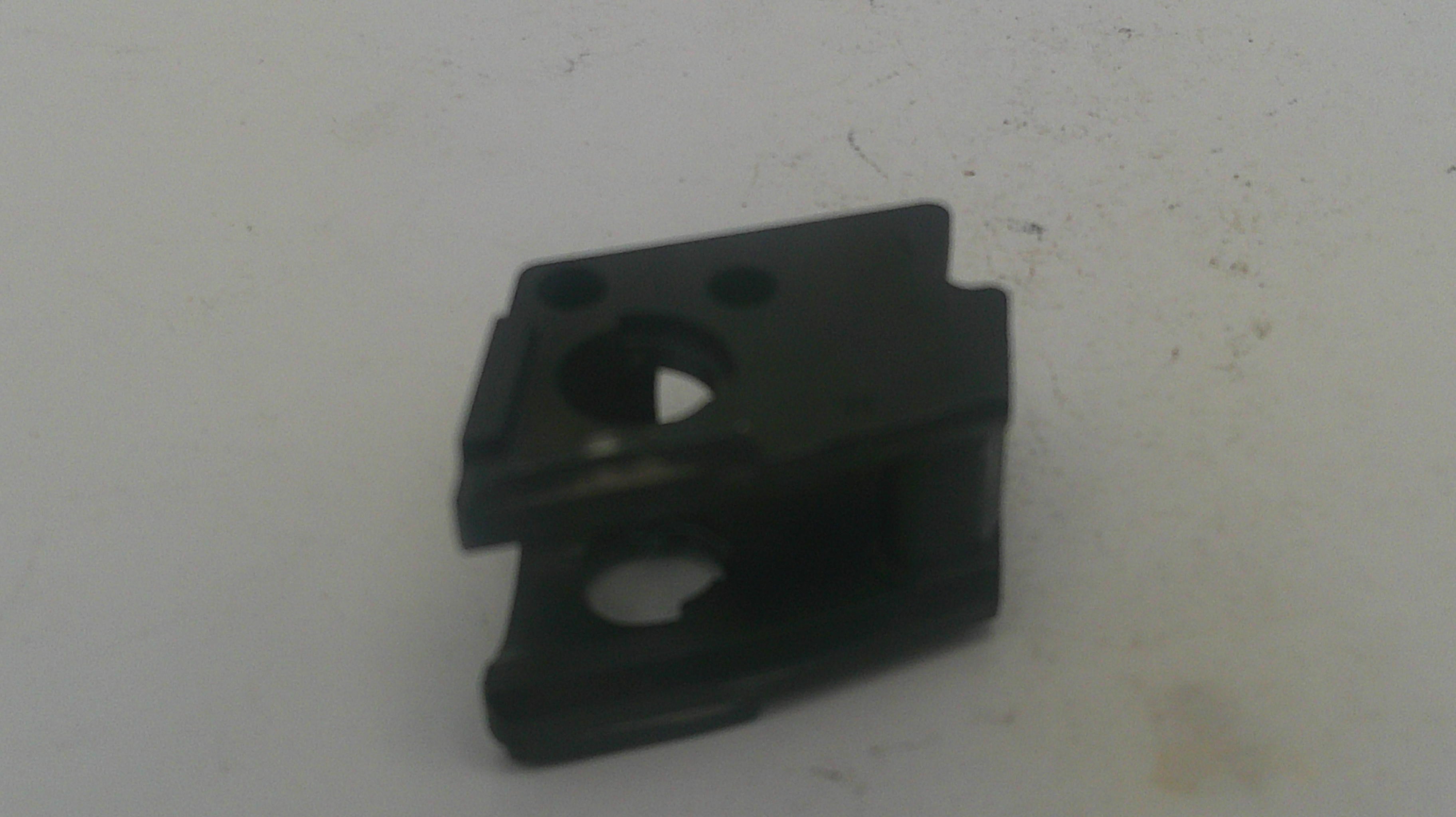 A small black plastic mechanical component or clip with circular cutouts, photographed on a plain off-white surface.