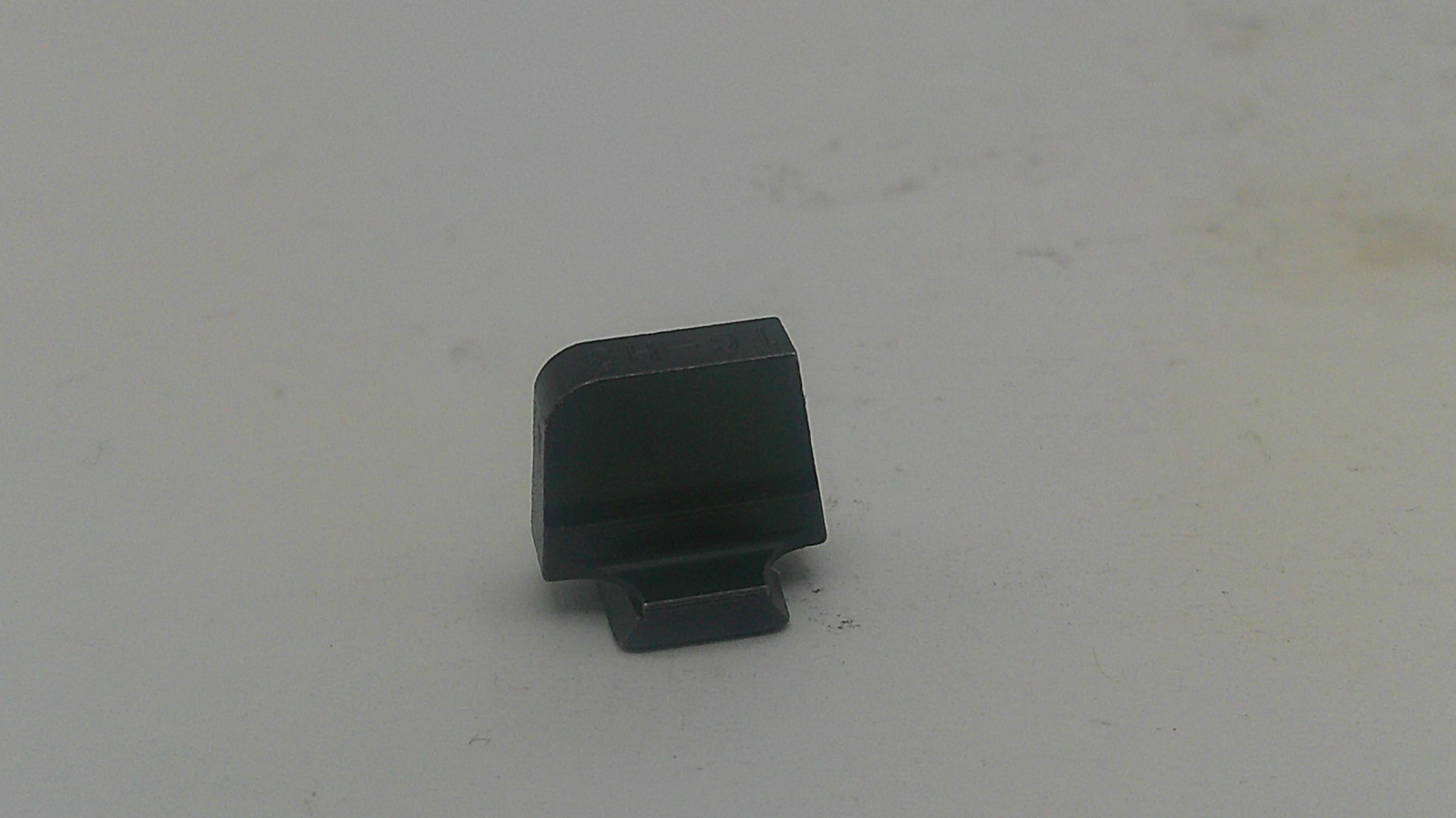 A small black plastic component, possibly a lens protector or cap, standing upright on a light gray surface.