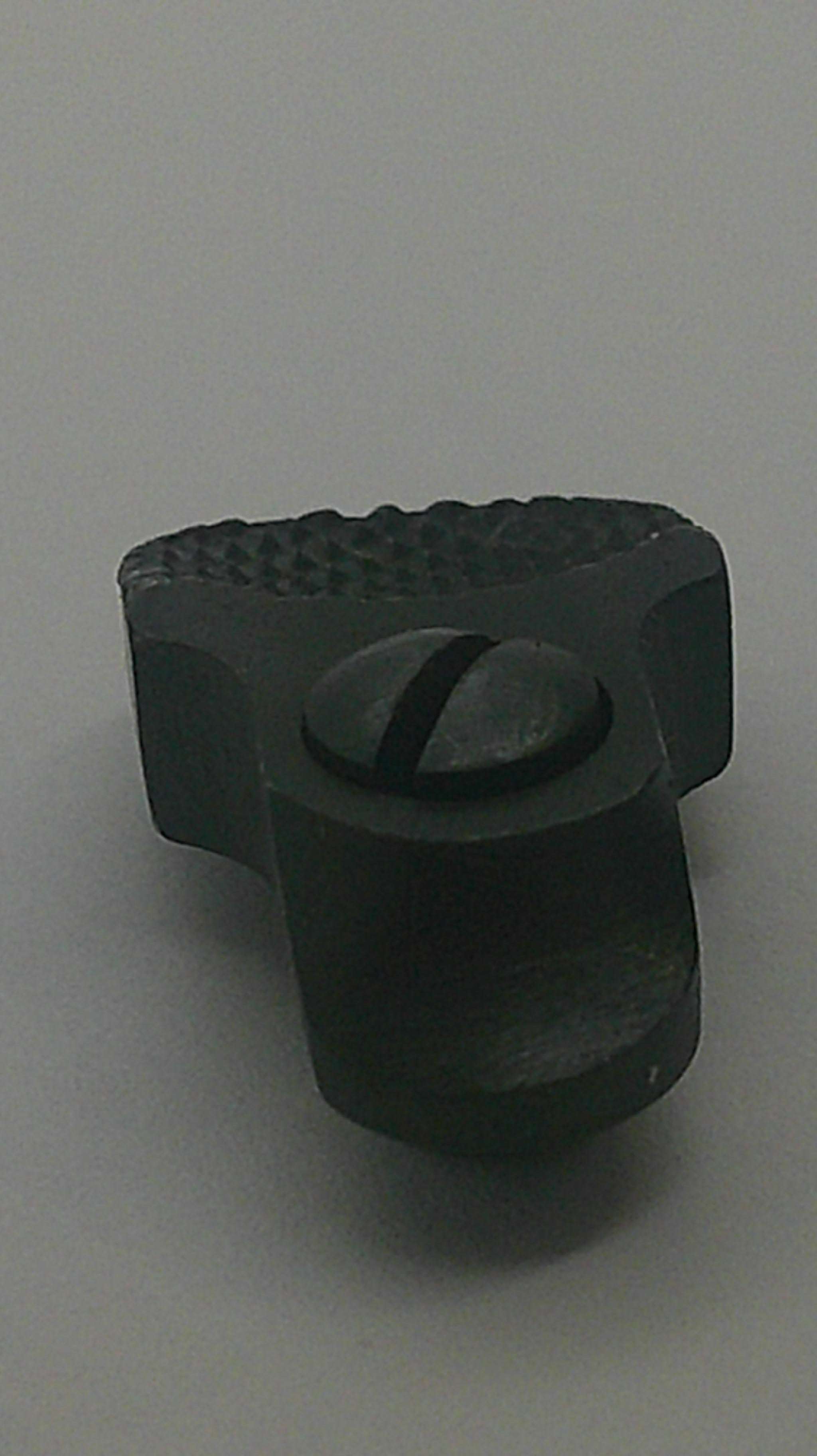 A small black plastic knob or dial with a textured side and a central oval cutout, photographed on a plain light gray background.