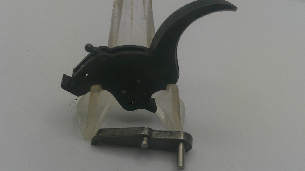 A black metal trigger assembly with a curved lever and a small metal spring, shown on a light gray background.