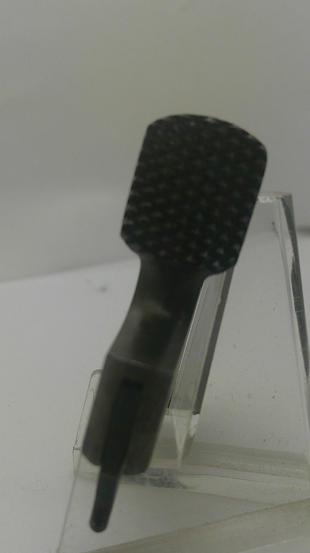 A black textured nail file or emery board with a pointed sharpened edge, mounted on a clear acrylic stand against a plain light background.