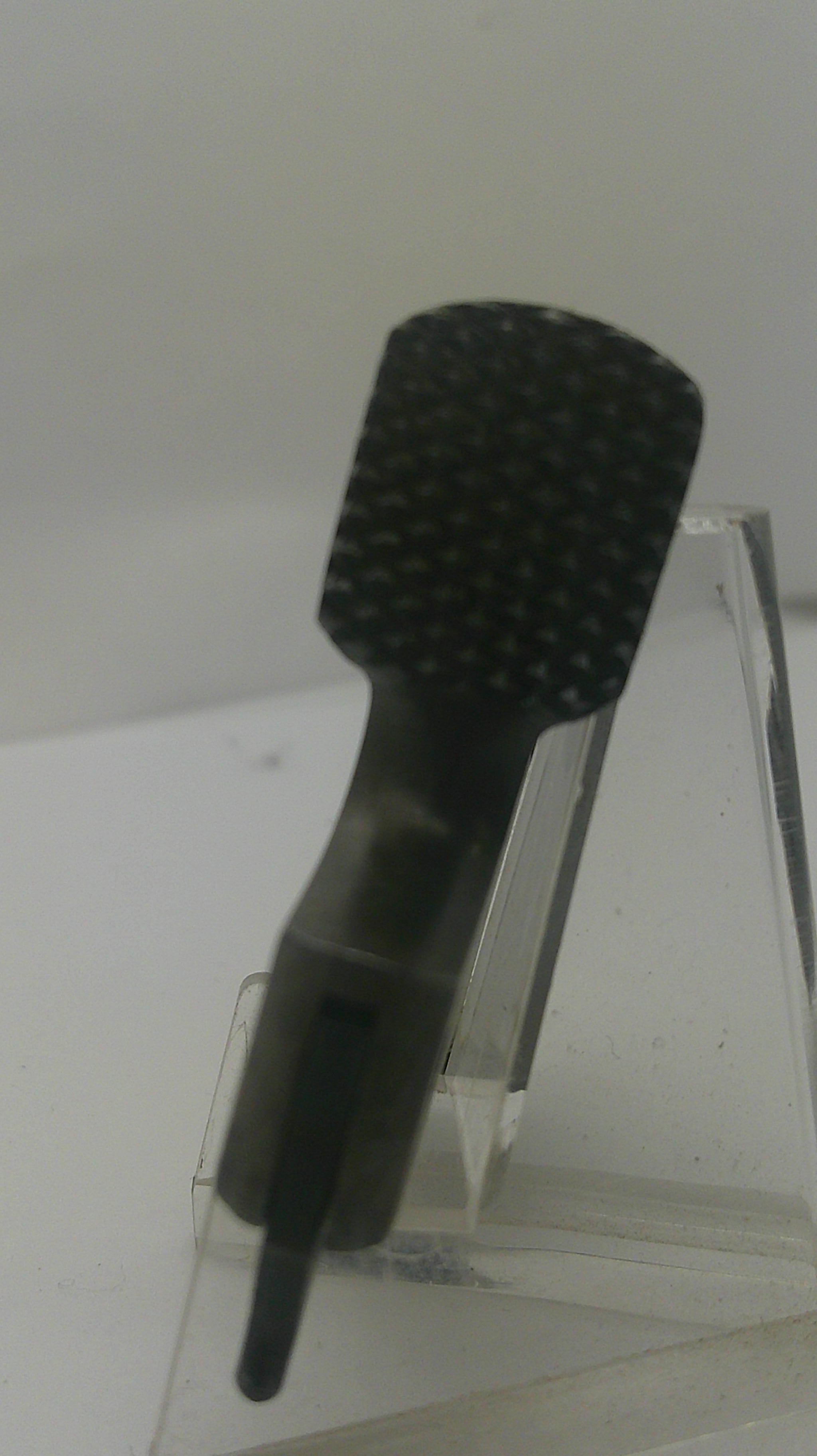 A black textured nail file or emery board with a pointed sharpened edge, mounted on a clear acrylic stand against a plain light background.