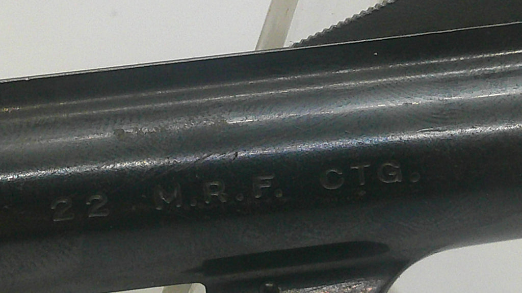 Close-up of a black metal firearm barrel section with embossed text reading '22 M.R.F. CTG.' on a plain light background.