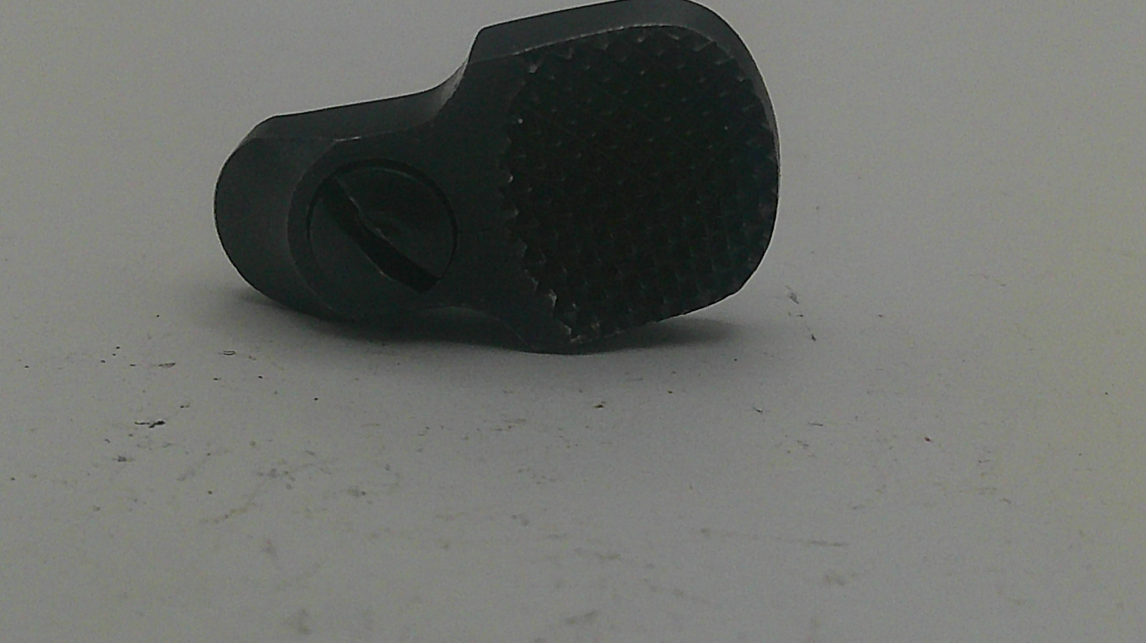 A black plastic cylindrical component with a textured circular end and a small side tab, photographed on a plain light gray surface.