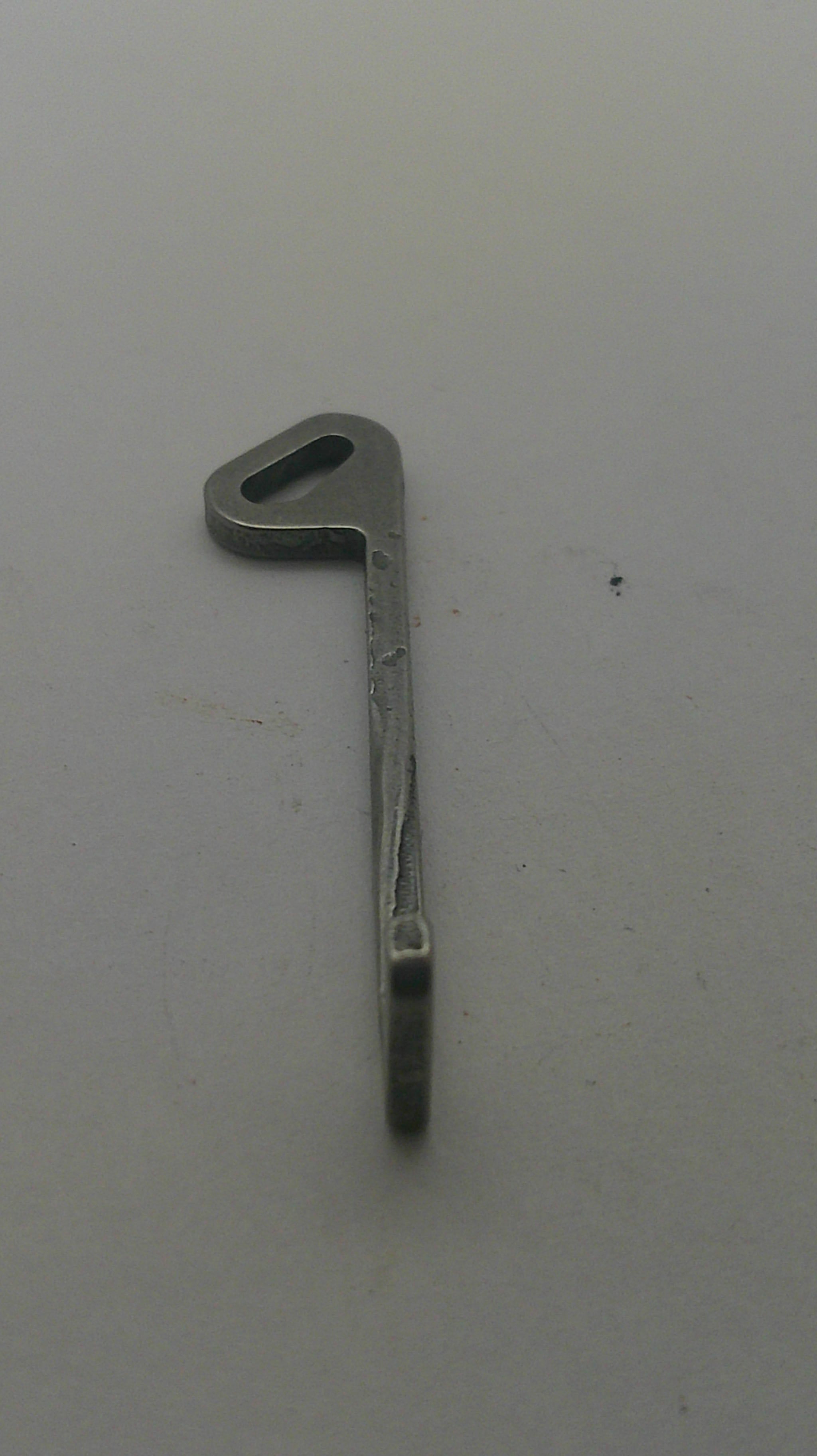 A small metal latch or bracket with a flat head and a slot cutout, shown on a plain light gray surface.