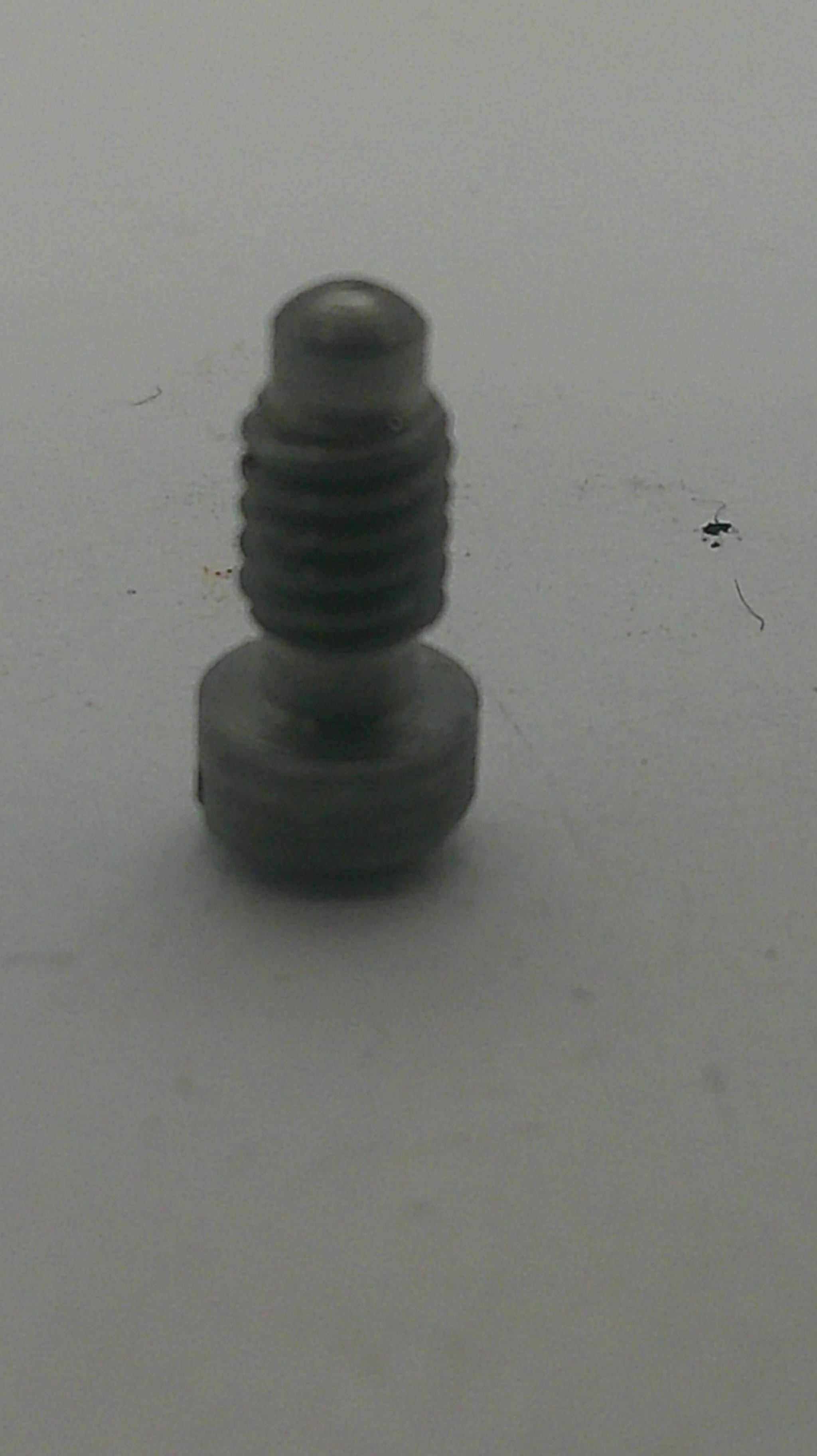 A small dark gray plastic or metal screw with a threaded shaft and a hexagonal head, shown on a plain light gray background.