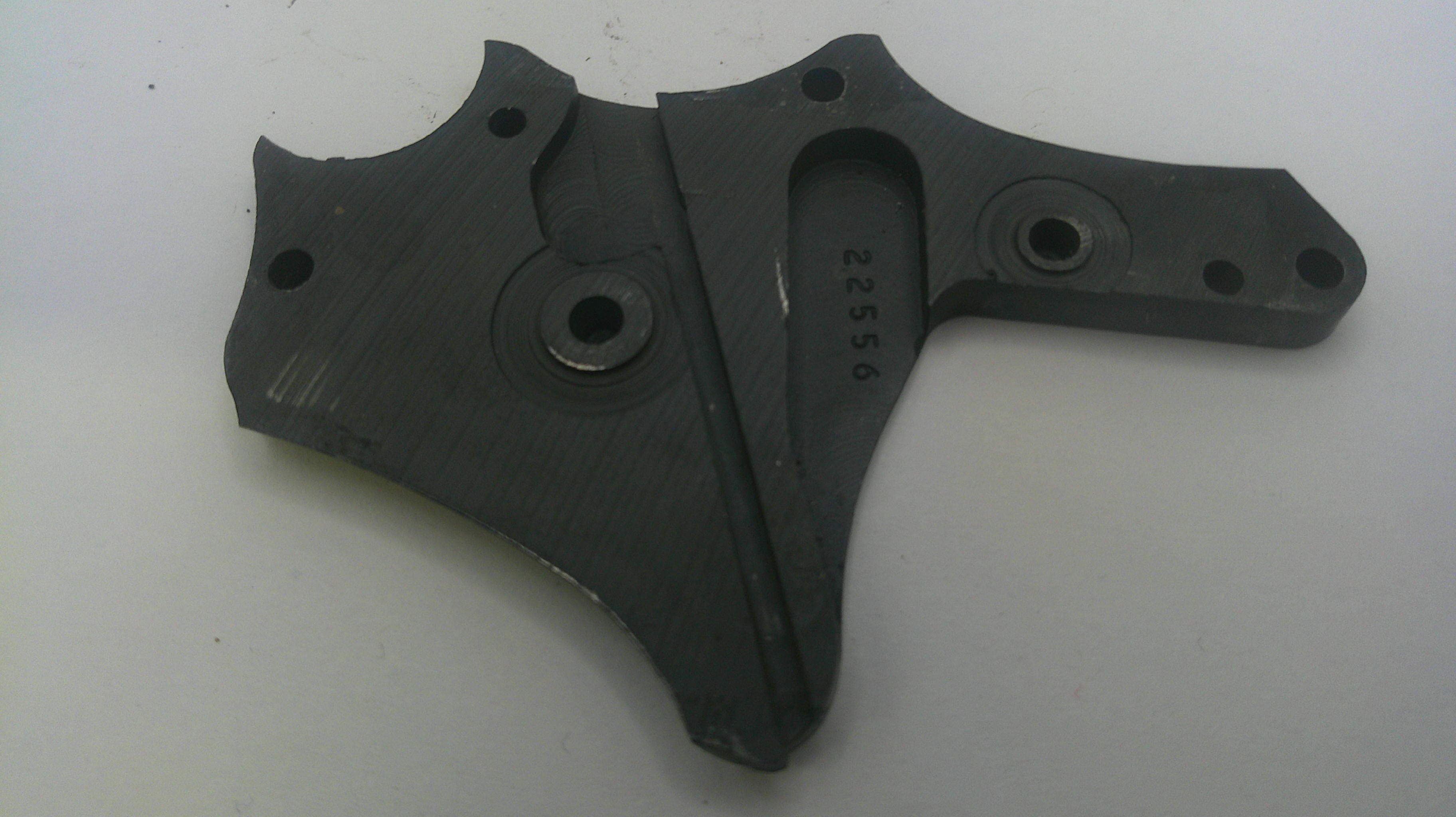 A dark gray cast metal mechanical part with pre-drilled mounting holes and stamped serial numbers, shown on a plain light background.