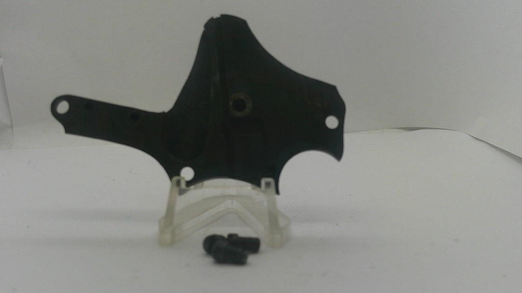 A black plastic mounting bracket or cover with pre-drilled holes, displayed on a clear plastic stand with two small black screws in front, set against a plain white background.
