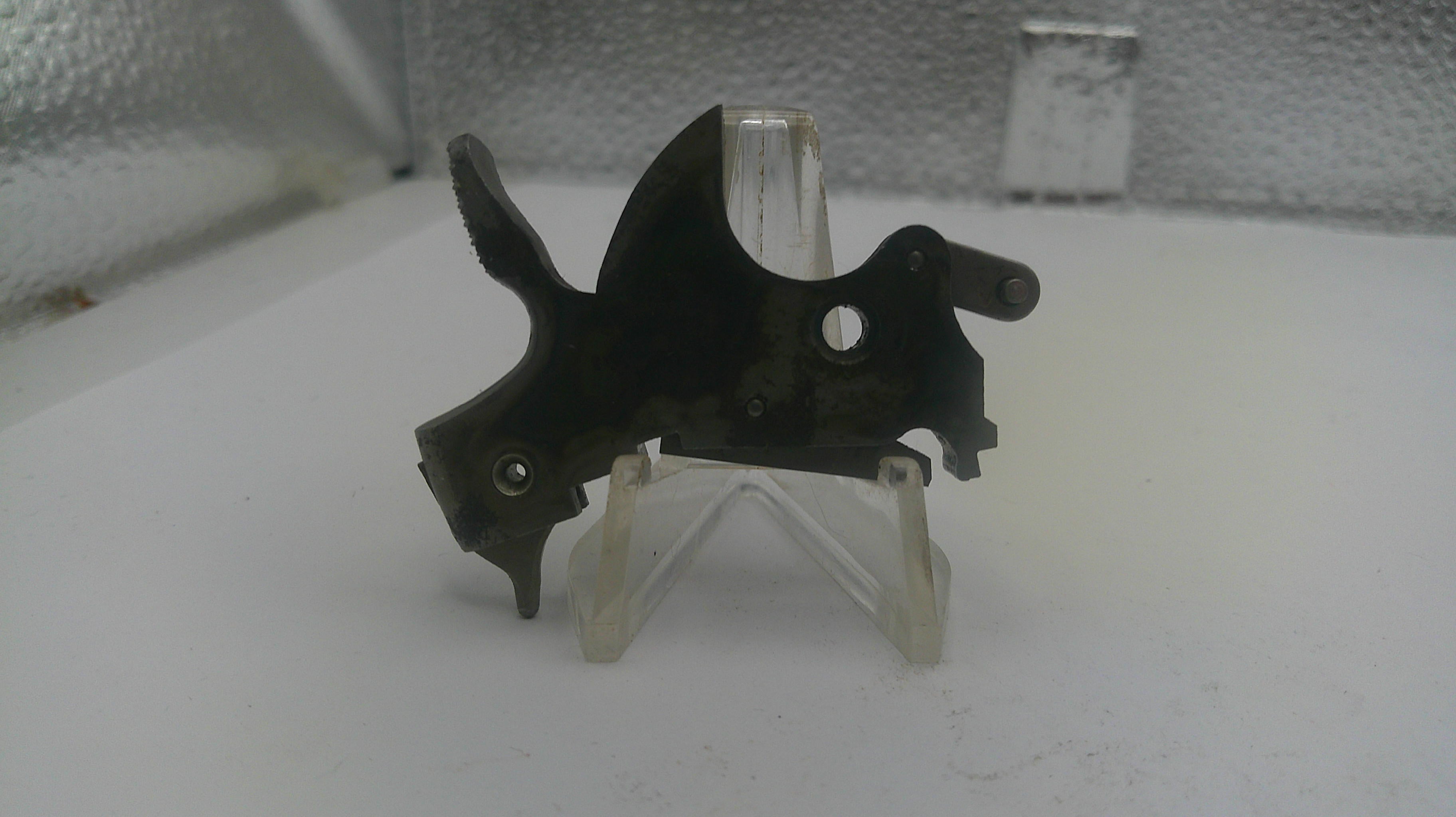 Black metal component on a white stand with a textured gray background