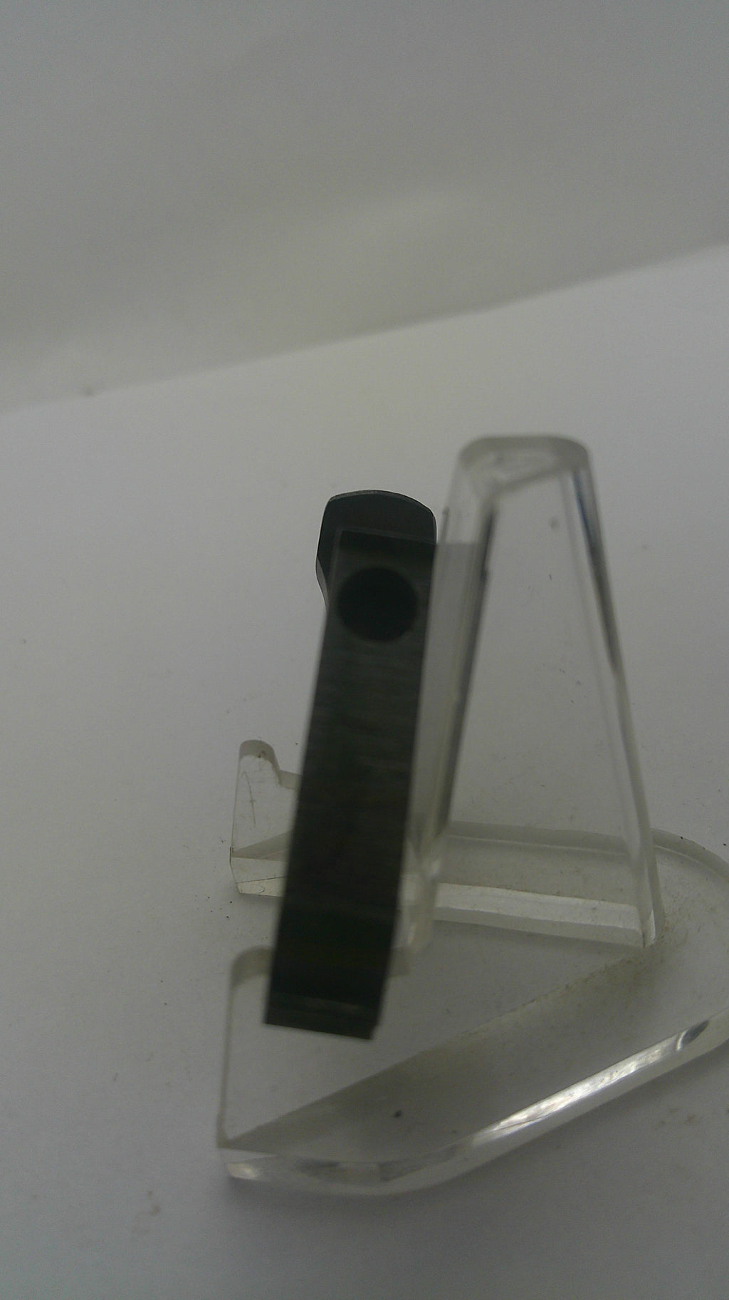 A black rectangular plastic component with a circular hole, mounted on a clear acrylic bracket against a plain white background.