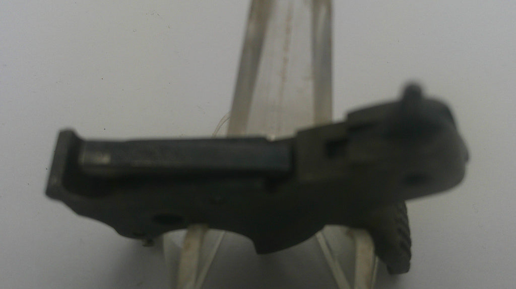 A small black plastic or metal component photographed against a plain light background, held by a clear plastic stand.
