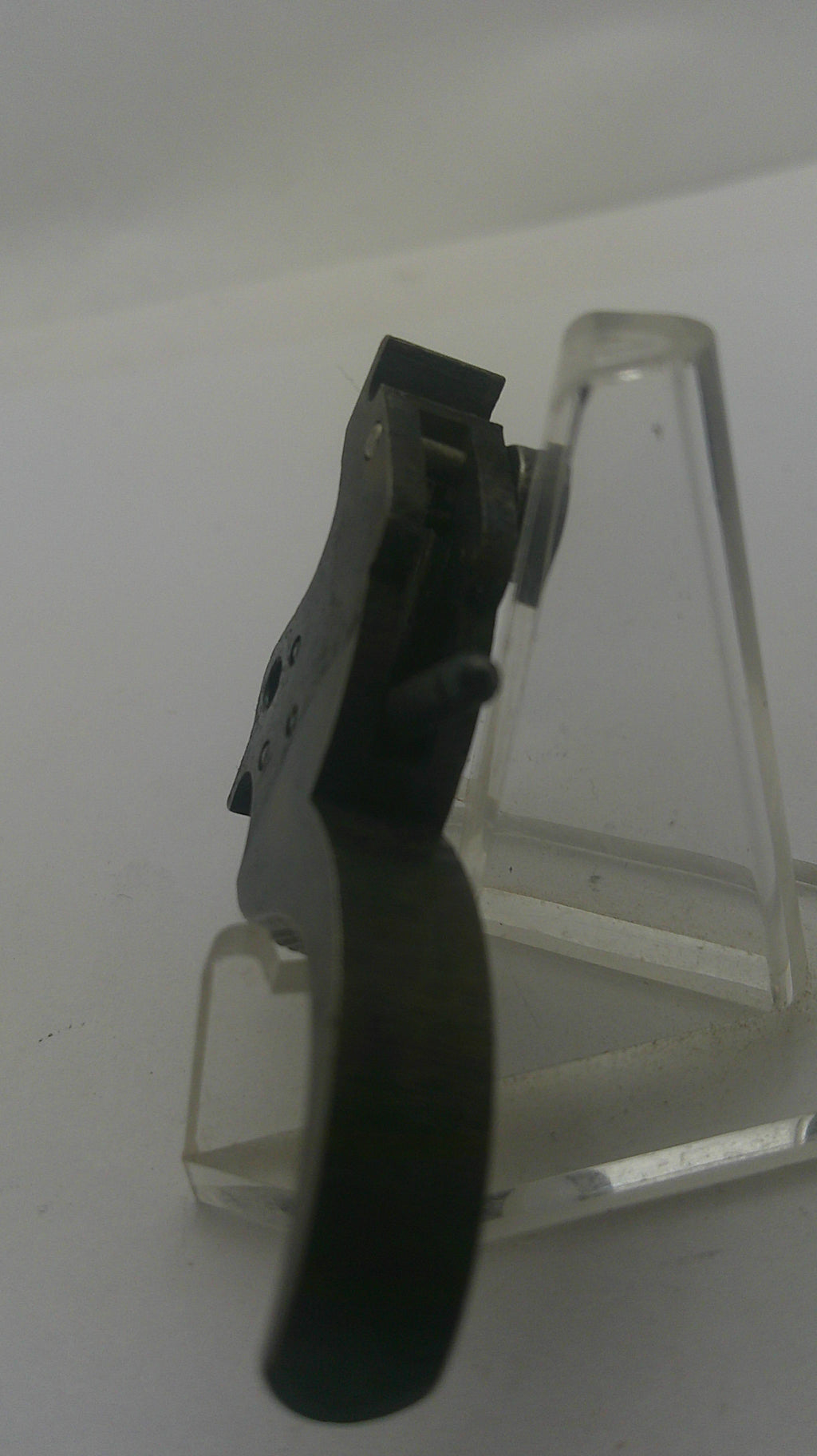 A close-up of a black plastic or metal tool mounted on a clear acrylic stand against a plain light background.