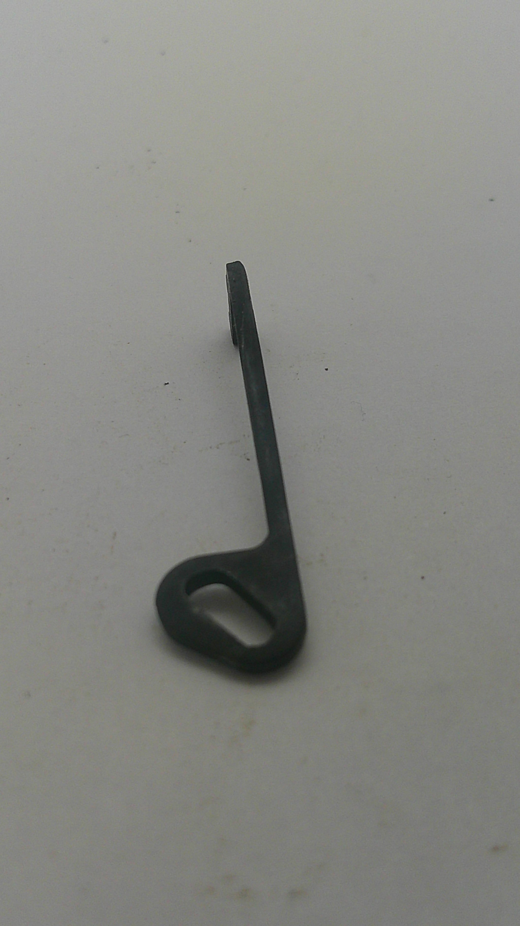 A small black plastic or metal hook with a looped end and a flat pointed stem, photographed on a plain off-white surface.
