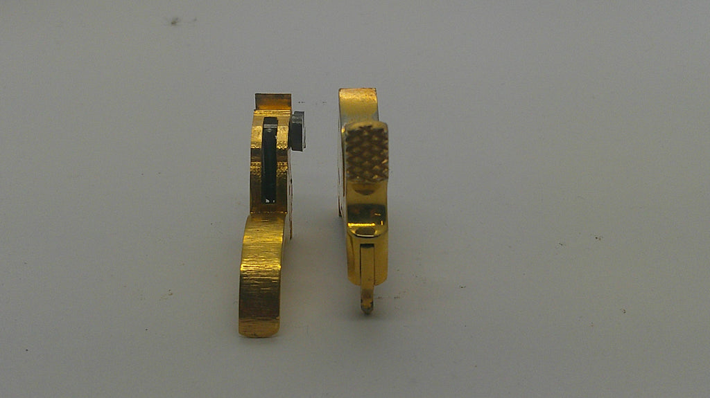 Two small gold-toned metal watch or gear components standing upright on a plain light gray background.
