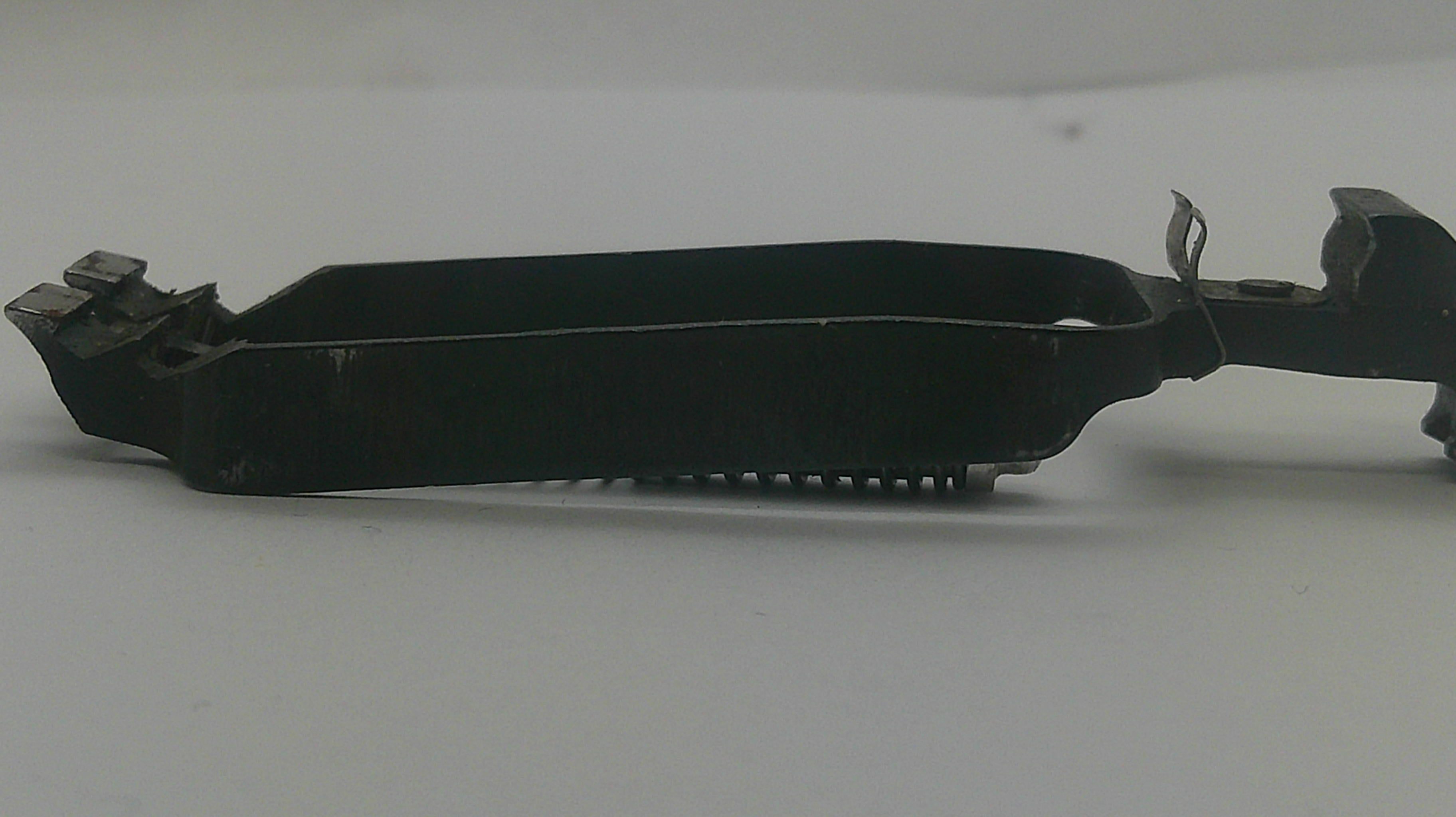 A black metal mechanical component or bracket with a rectangular opening and small protruding teeth on one end, shown on a plain light gray background.