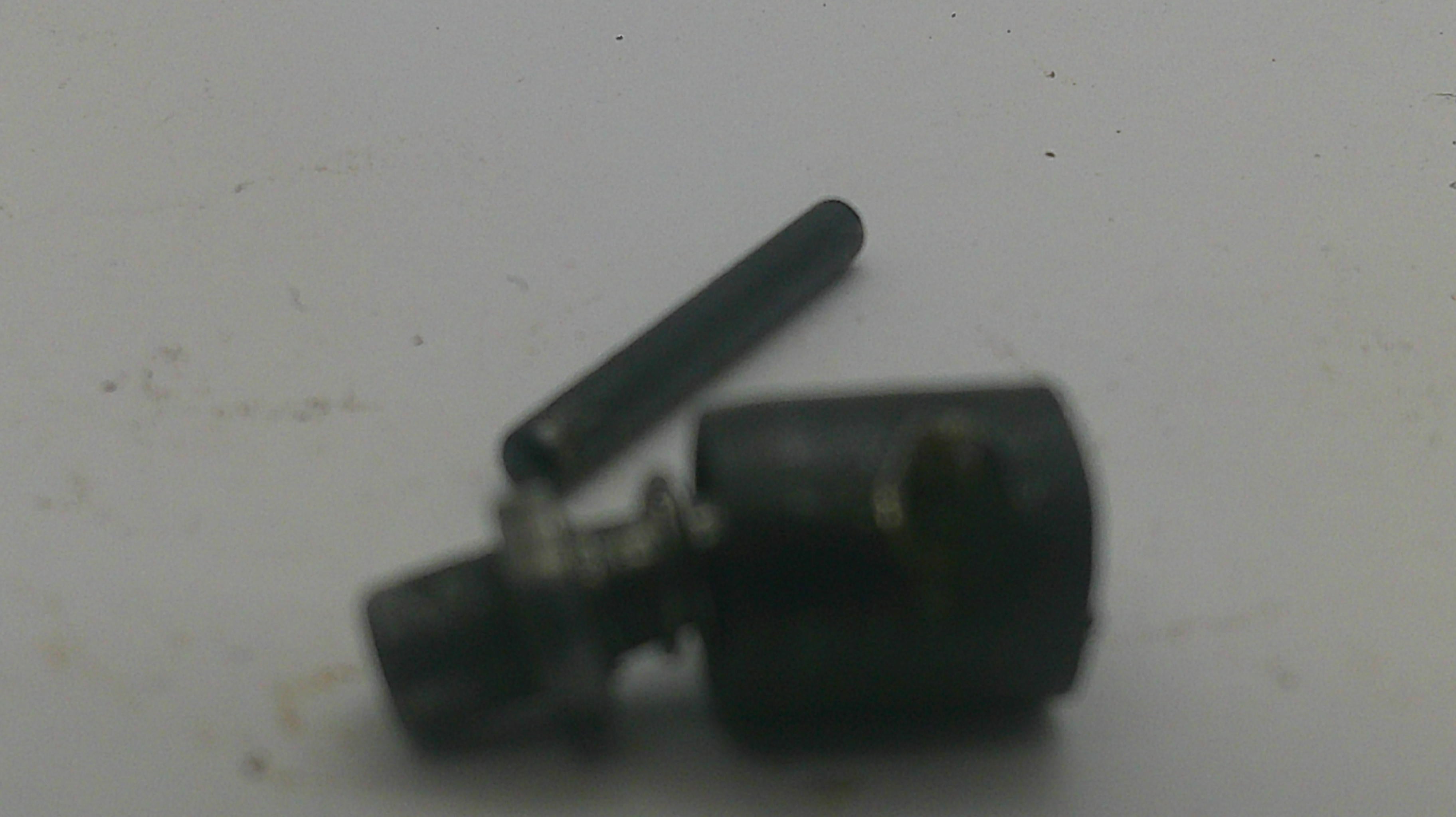 A small black metal mechanical component with a cylindrical body and a separate matching pin, photographed on a plain off-white surface.