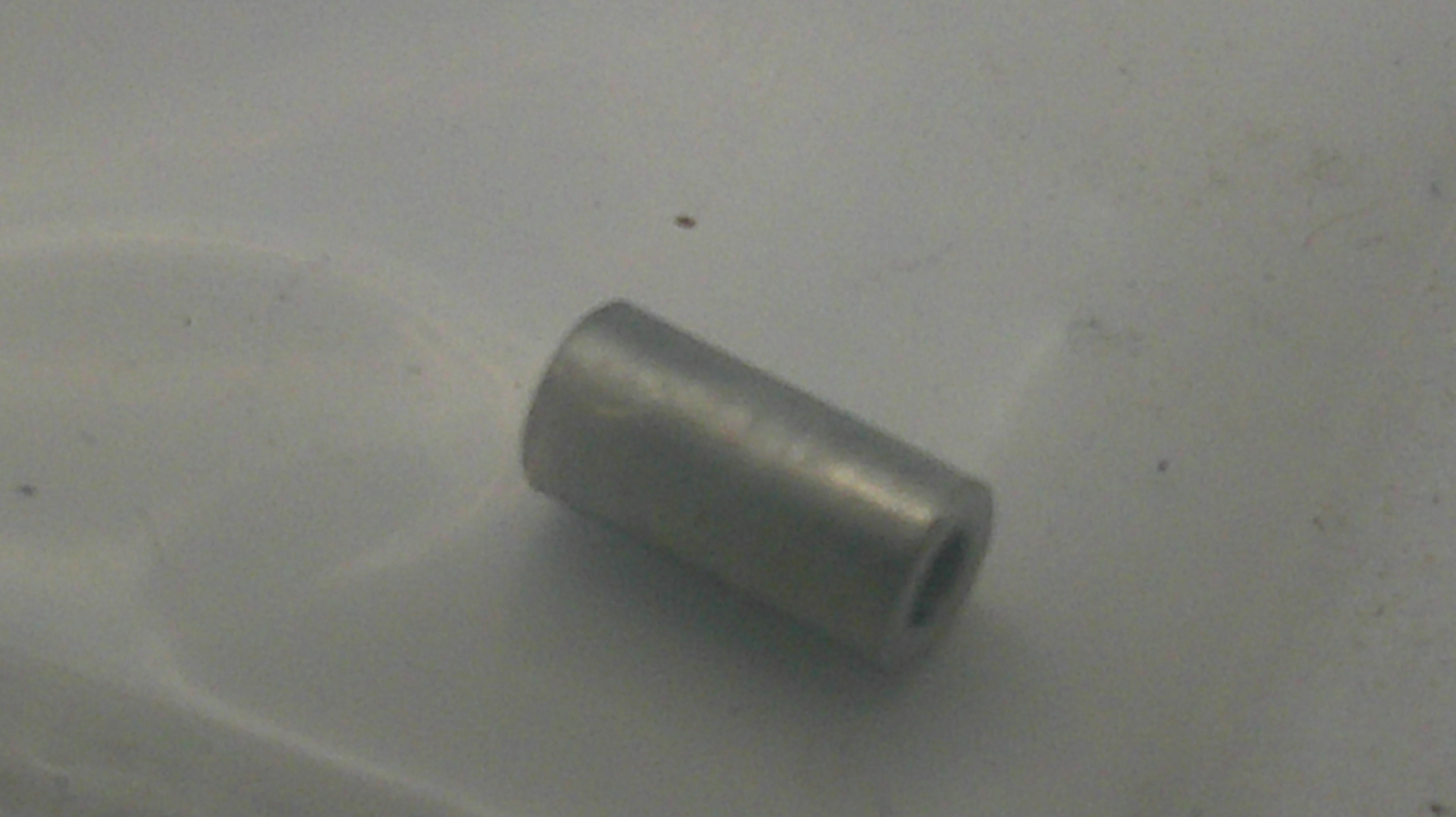 A small metallic silver cylindrical bead with a hollow center, resting on a light gray surface.