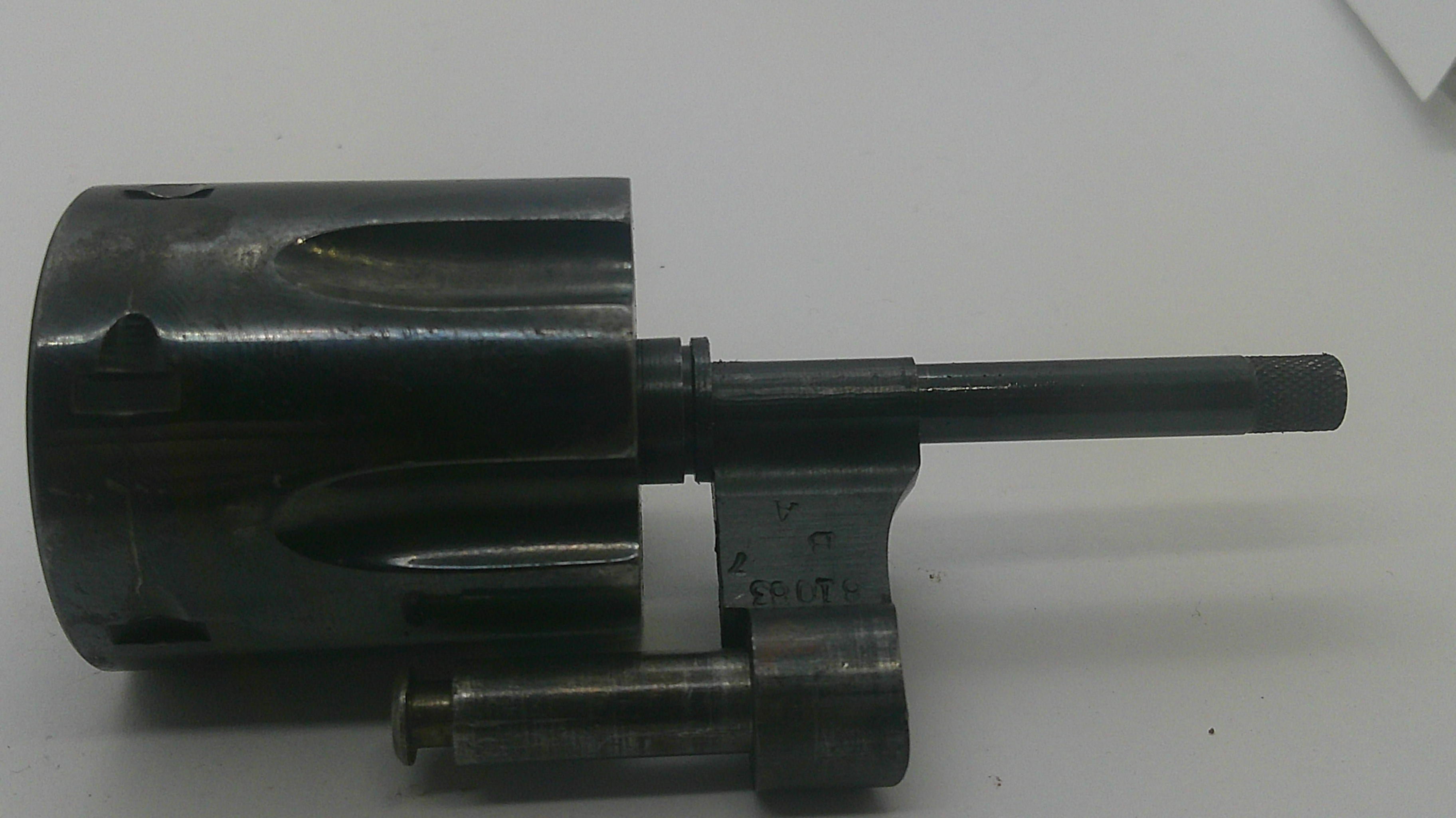 A used dark gray metal mechanical component, possibly a valve or pump part, with a cylindrical body, a long horizontal rod, and a smaller vertical rod, photographed on a plain white surface.