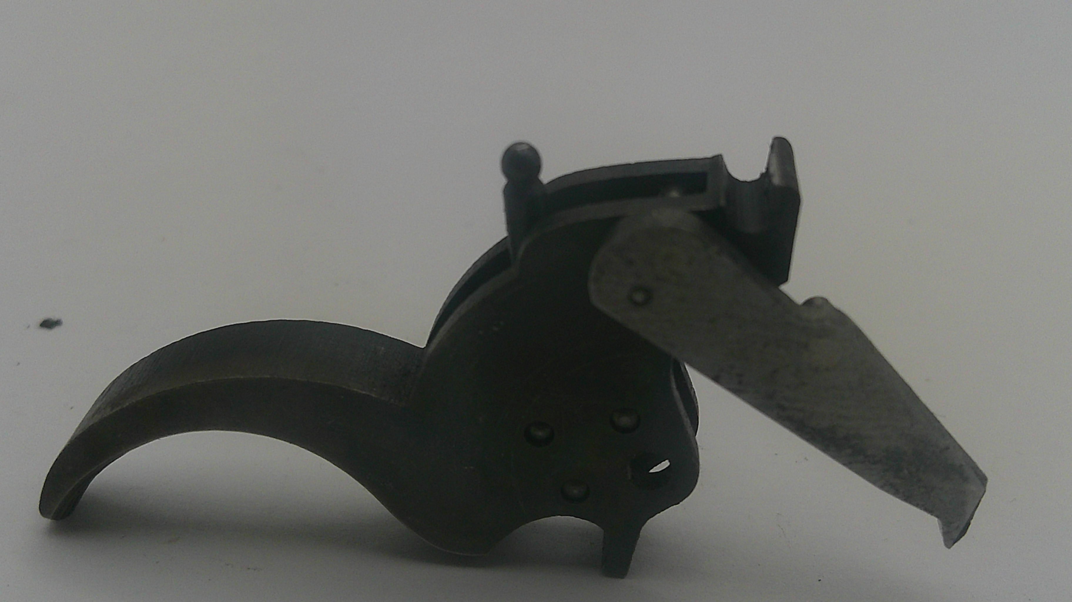 A dark metal firearm trigger assembly with a curved black handle and a silver-toned metal lever, photographed on a plain light gray background.