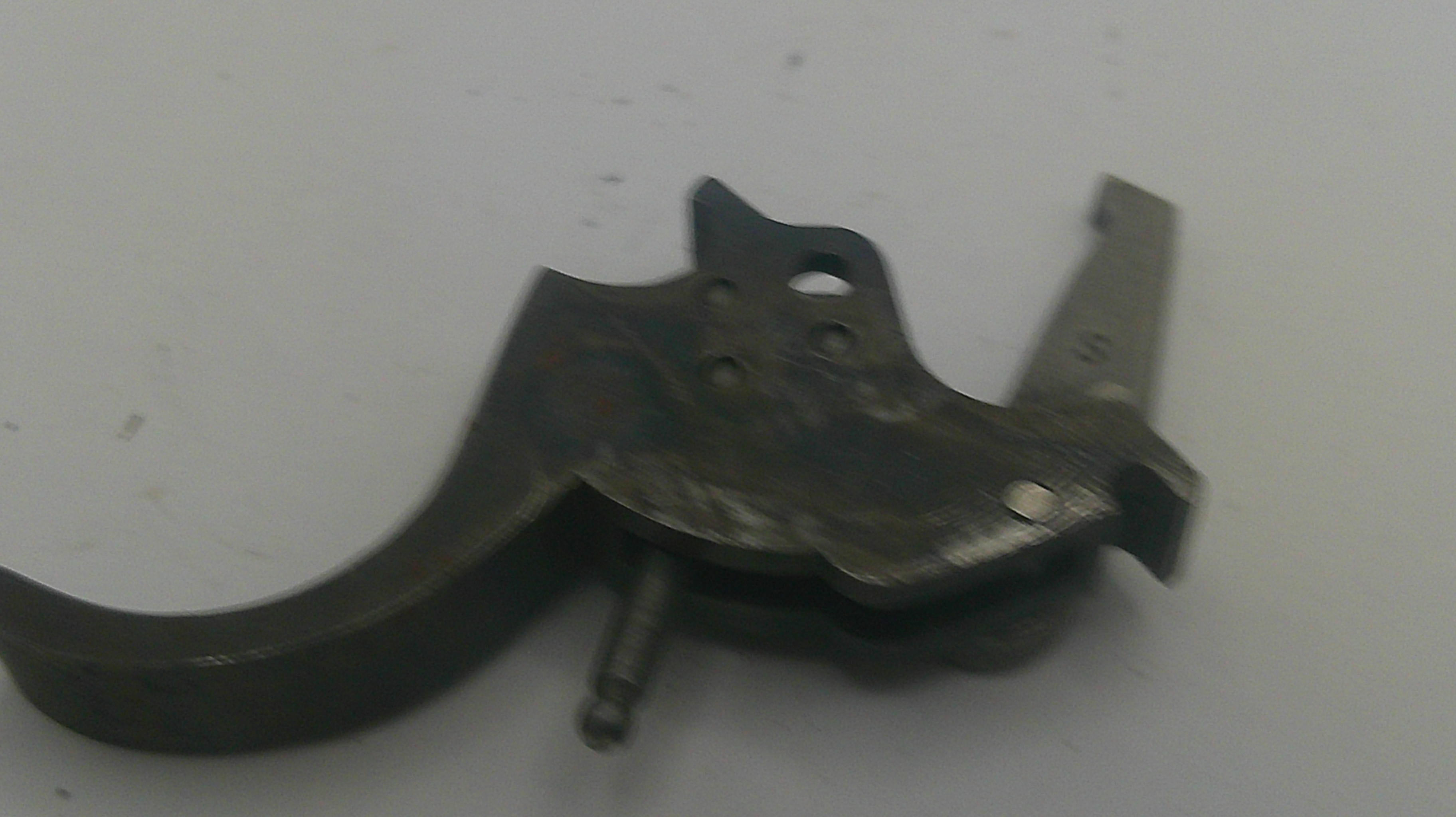 A dark metal firearm trigger assembly component, photographed on a plain light gray background.