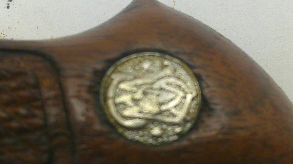 Close-up of a dark brown wooden object with a round metallic emblem featuring Arabic calligraphy, set against a light off-white background.