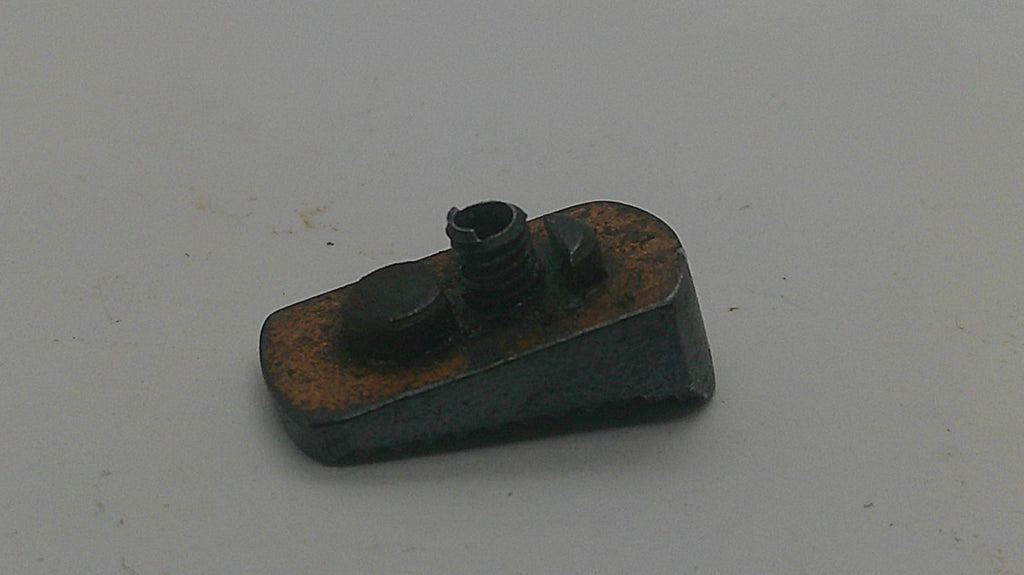 A small dark metal mechanical component with rusted orange-brown areas, photographed on a plain light gray surface.