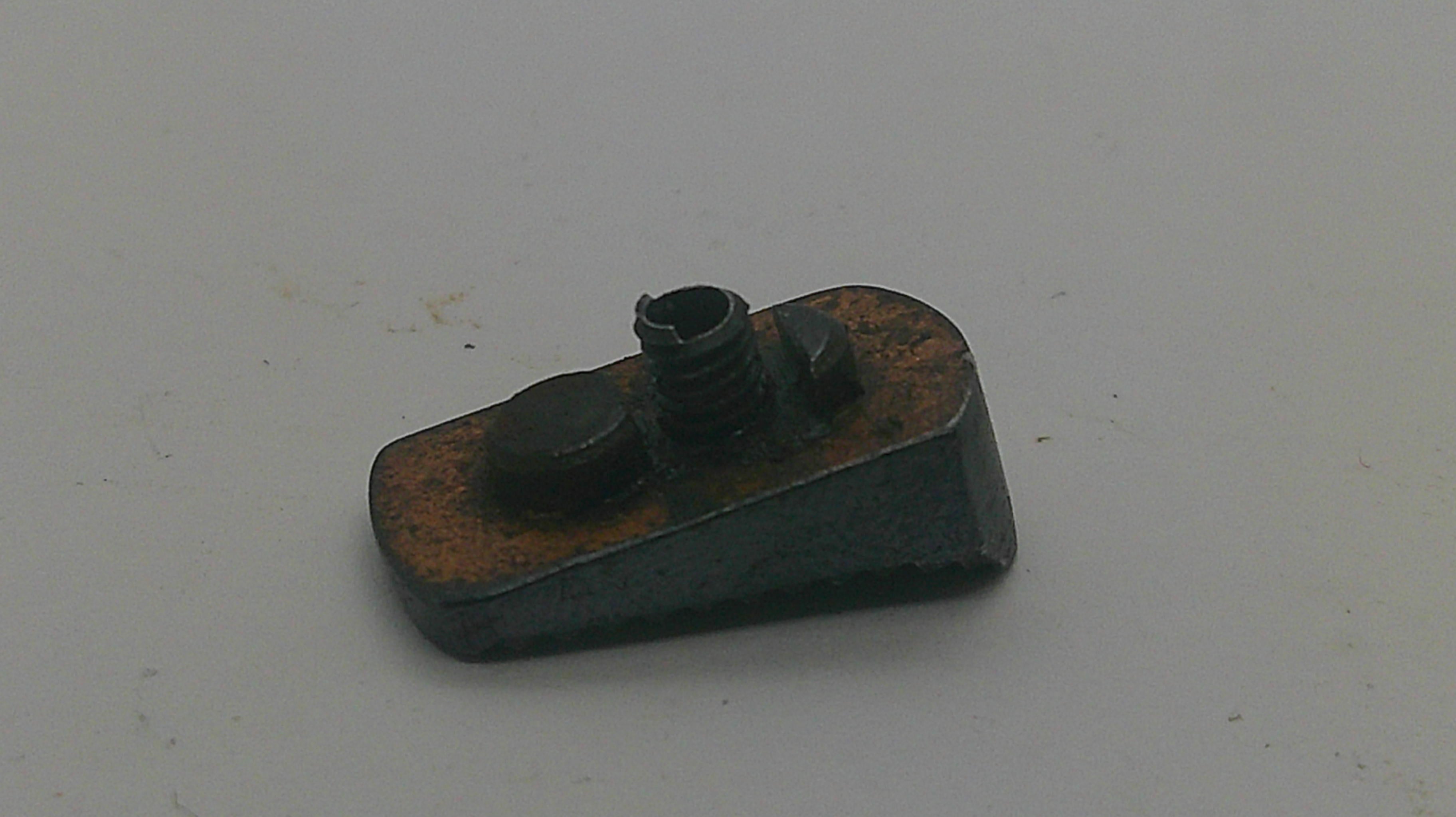 A small dark metal mechanical component with rusted orange-brown areas, photographed on a plain light gray surface.
